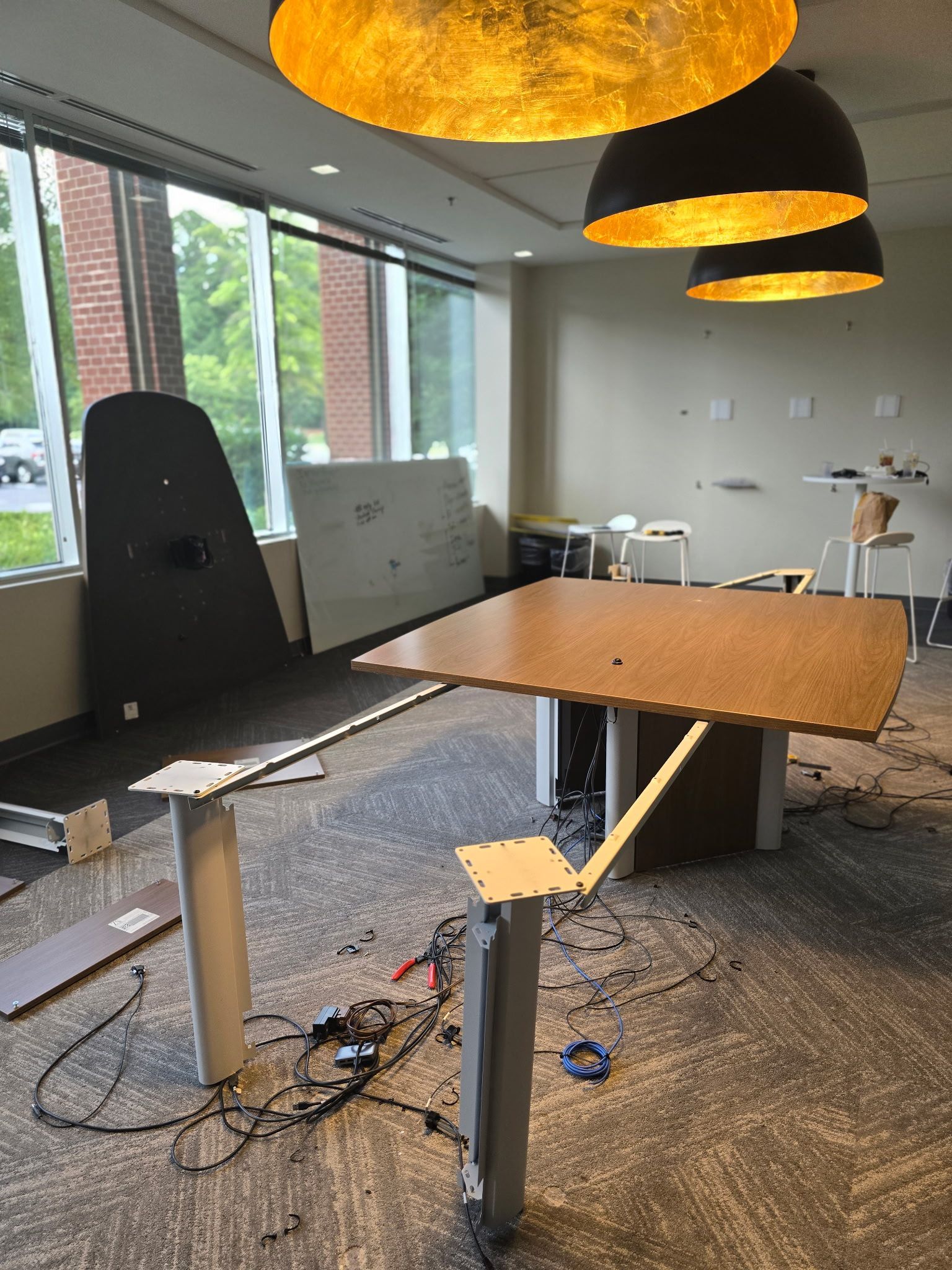 Office space with partially assembled desk and large windows. Lights hang from ceiling.