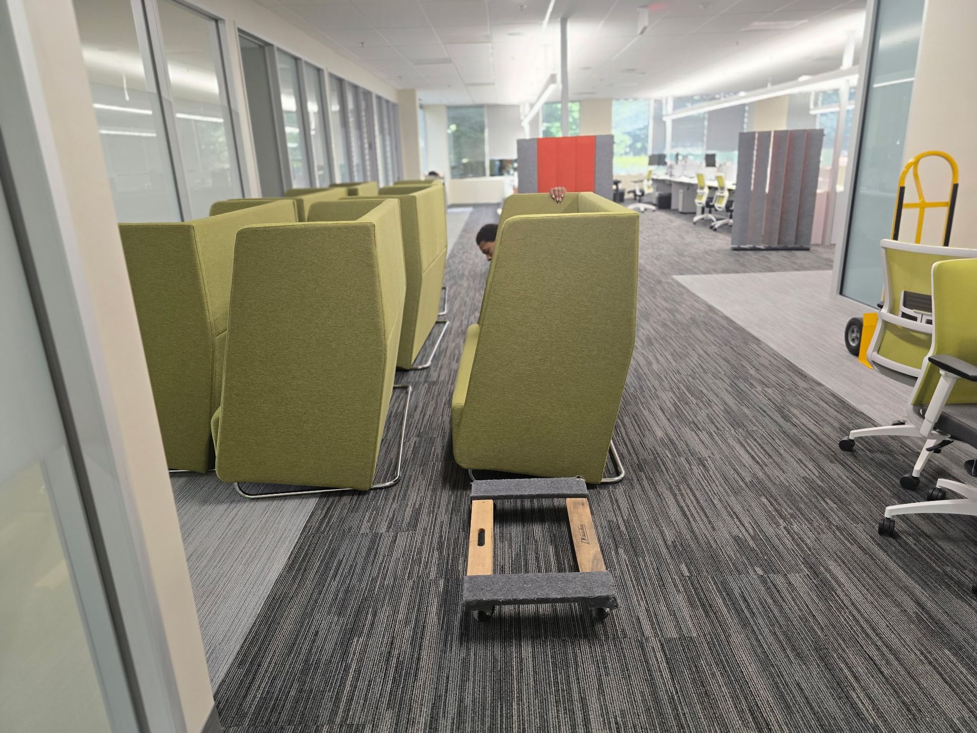 An office interior with movable green booth seating, a hand truck, and office furniture.