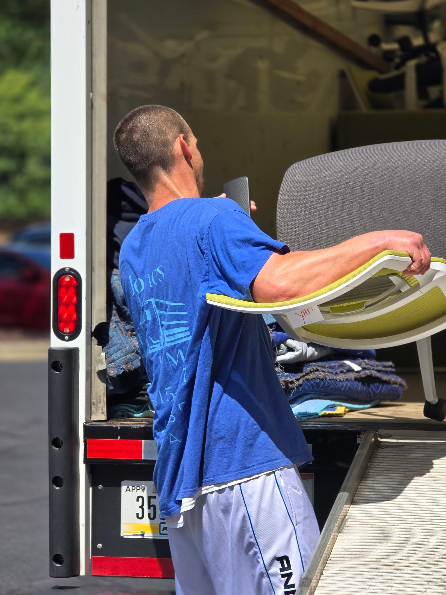 A person in a blue shirt is moving items out of a truck, carrying a chair, with the truck ramp visible.