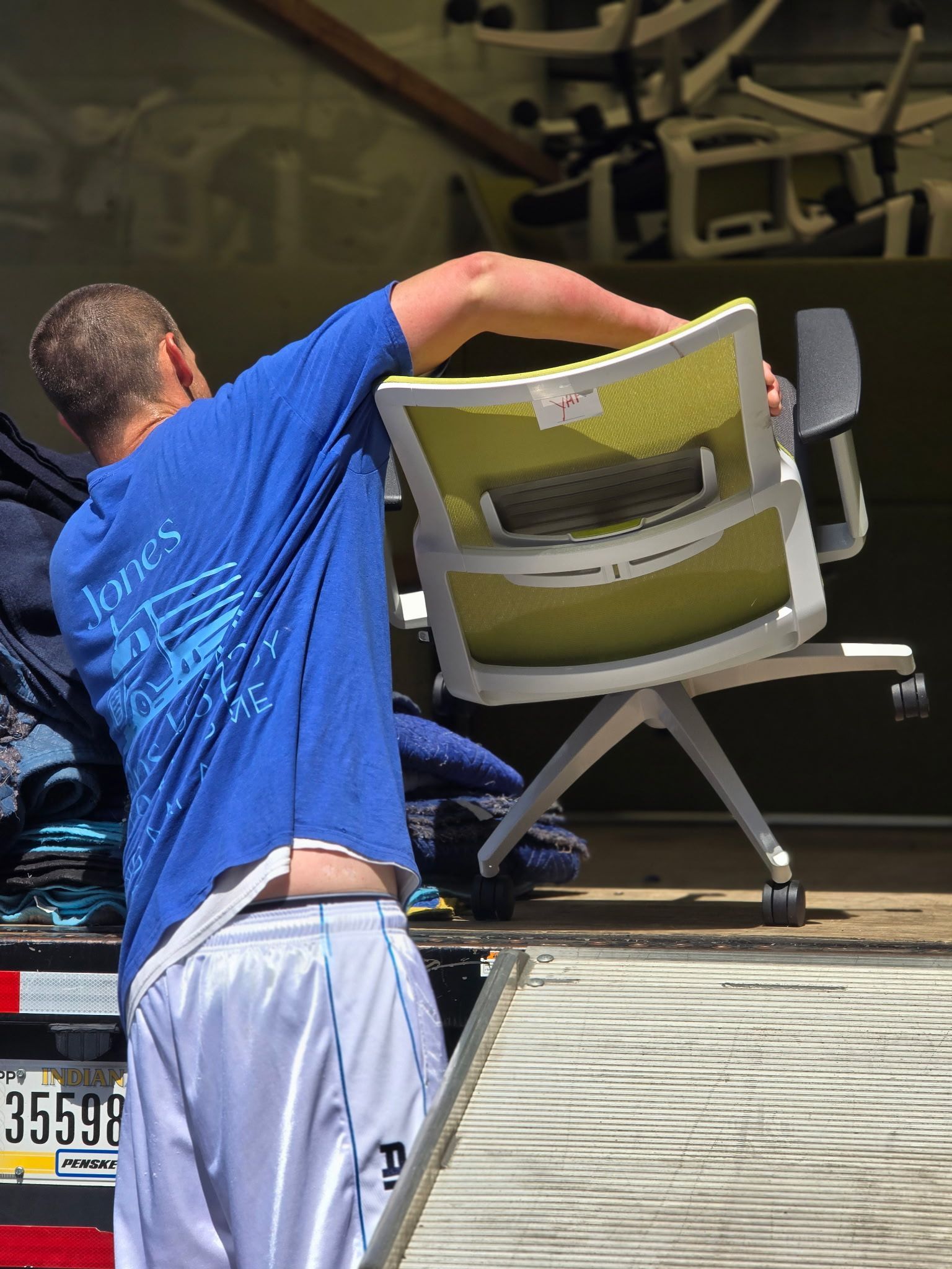 Man in blue shirt loading a yellow-backed office chair onto a truck.