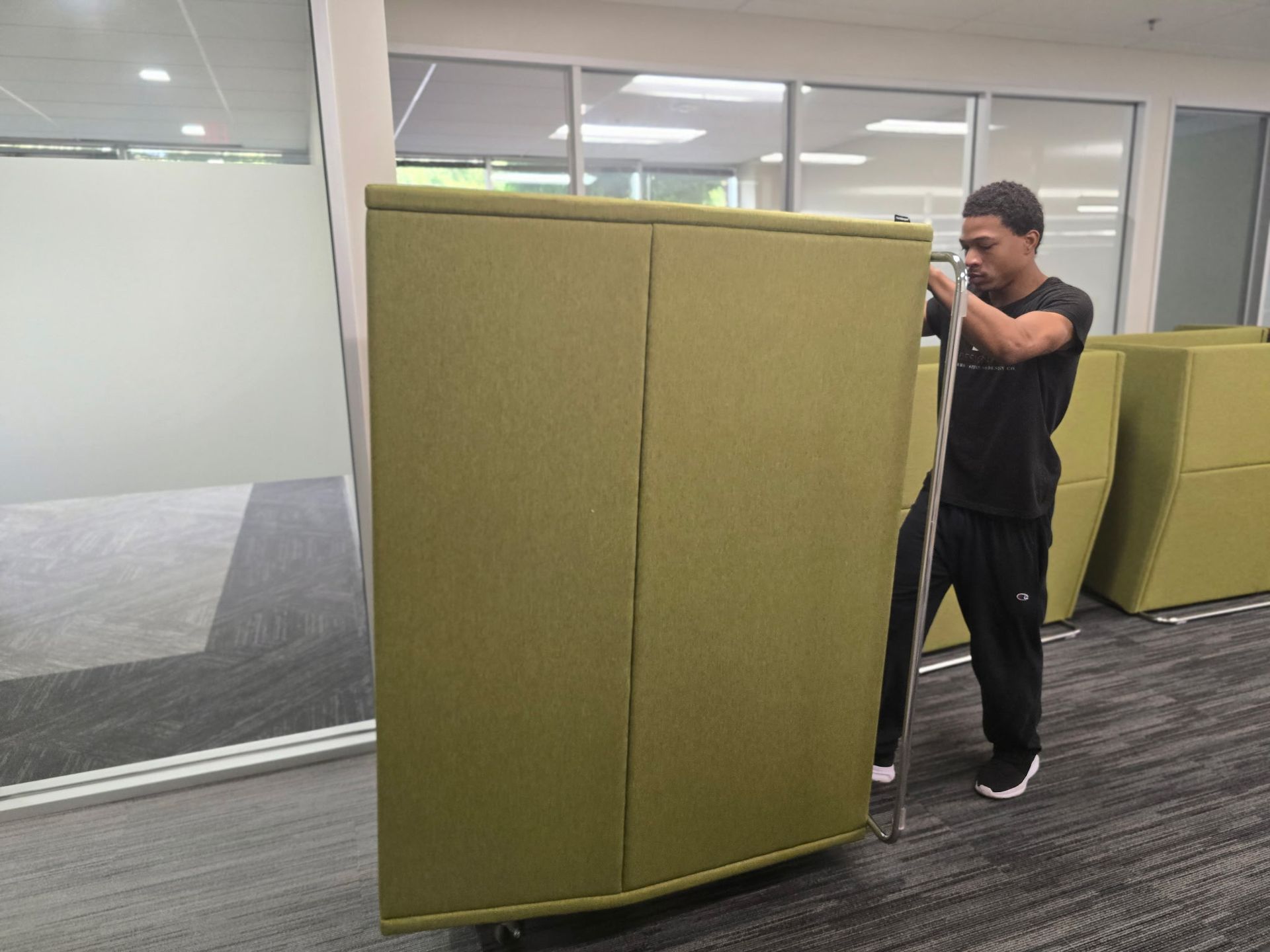 Man moving a large green partition on wheels in an office space.