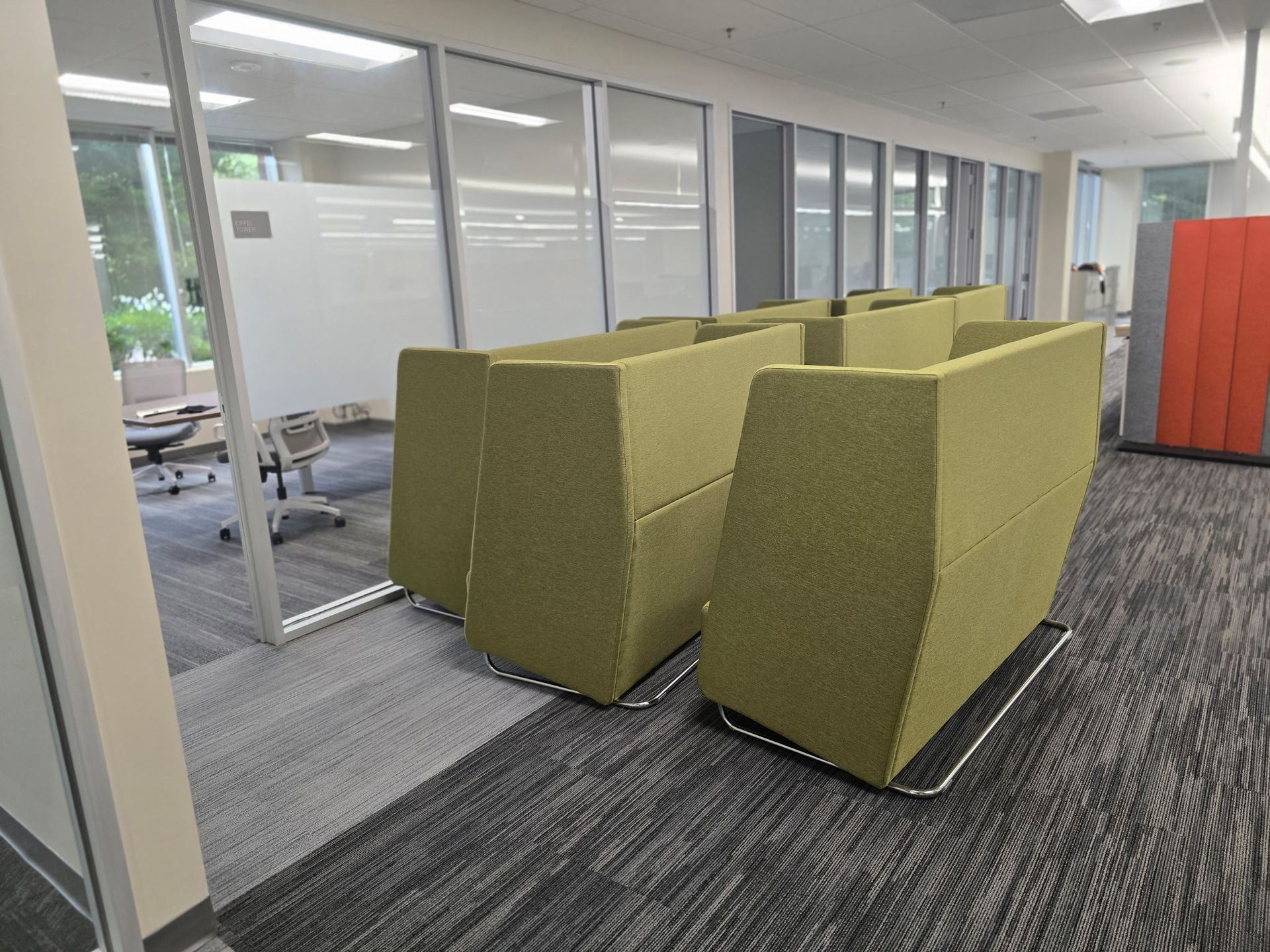 Office space with modular green seating, glass walls, and a patterned carpet.