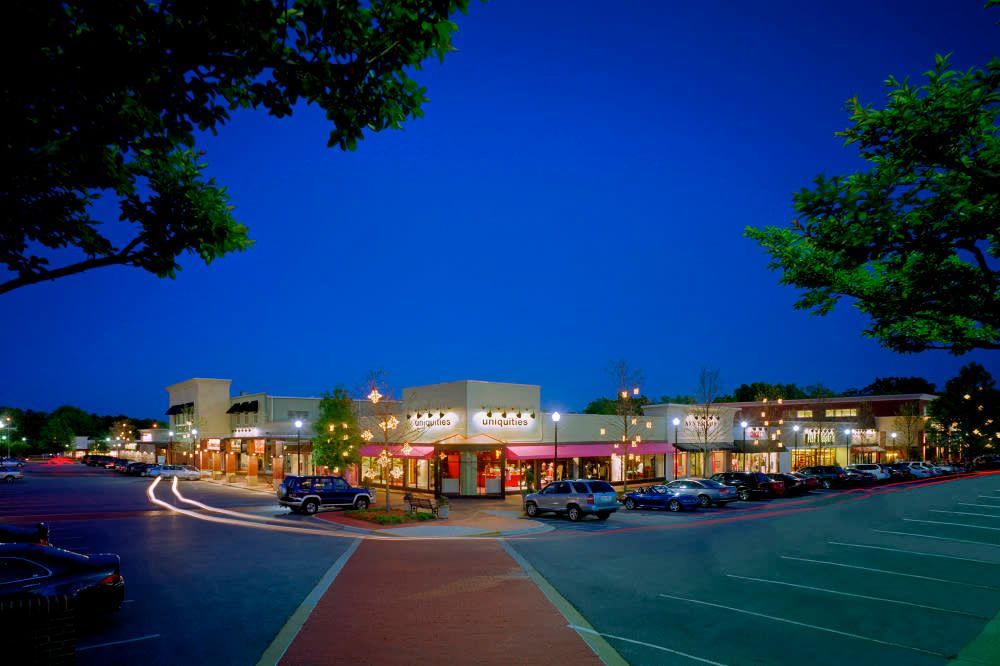 Village District Raleigh shopping center at dusk with stores lit up, cars, and blue sky.