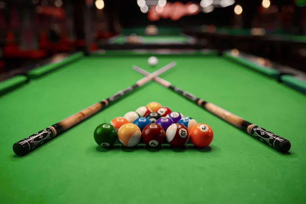 Close-up of a leveled pool table with cues and racked balls, signifying JHUM's experience assembling pool tables. ``