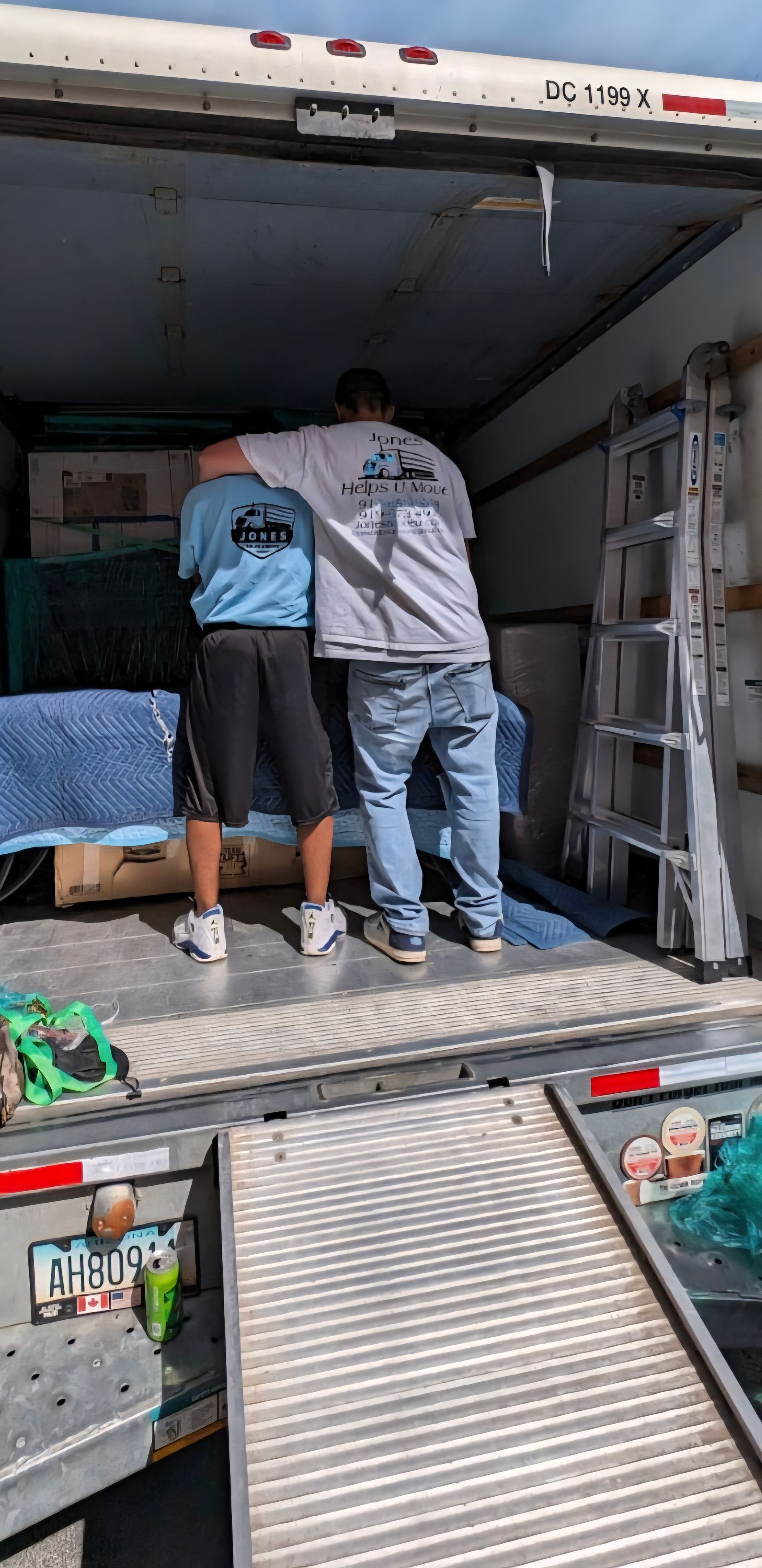 Two people inside a truck load furniture. One has an arm around the other's shoulders. A ramp is extending down.