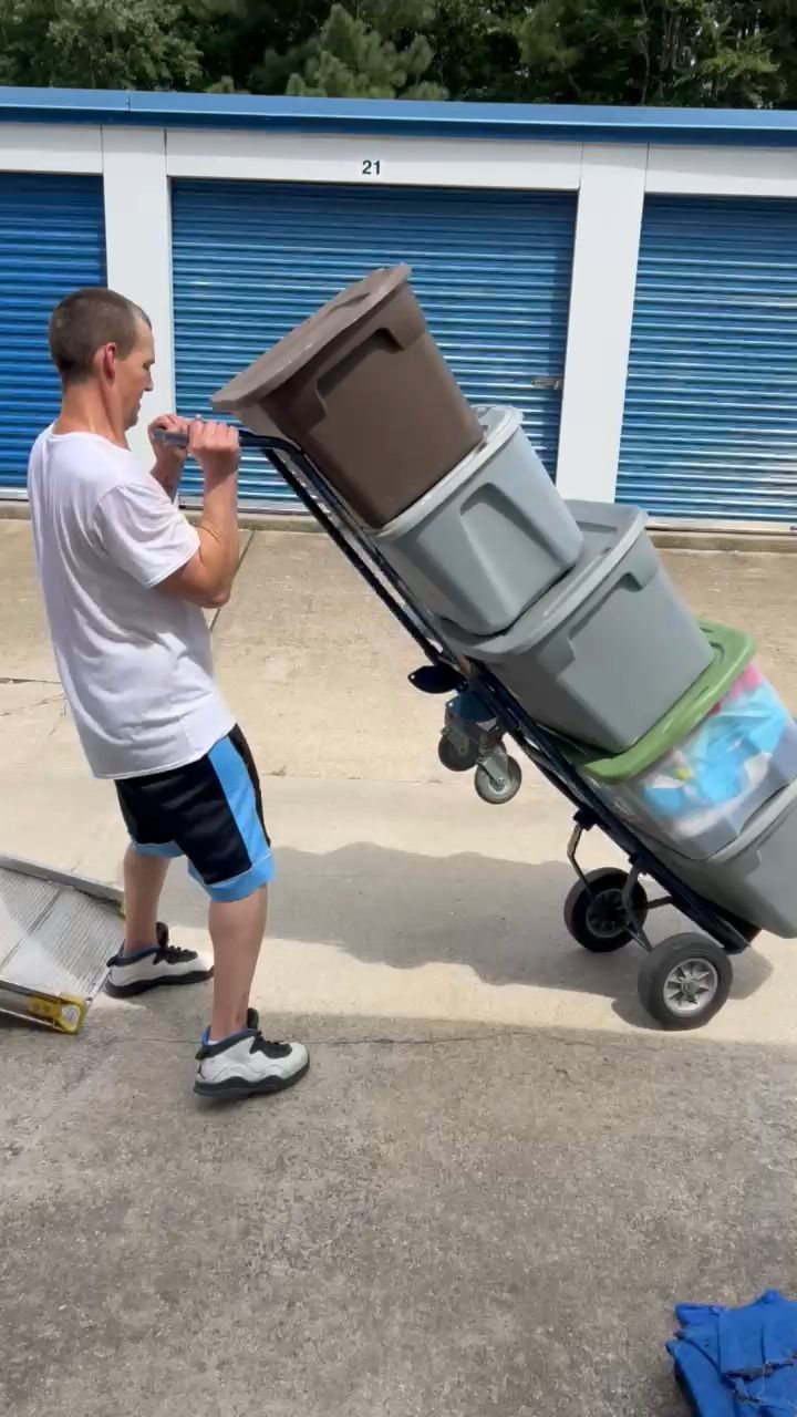 Man pulling a cart stacked with storage bins in front of storage units.