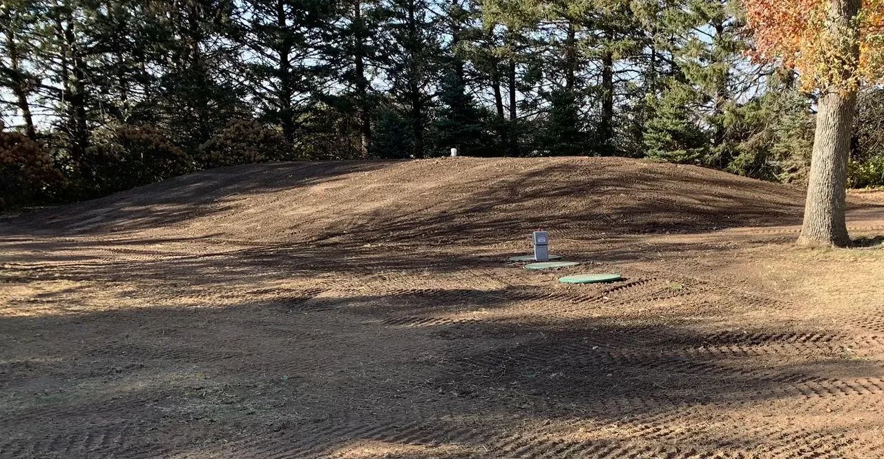 A dirt mound in an outdoor setting with trees in the background. Two markers are in the foreground.