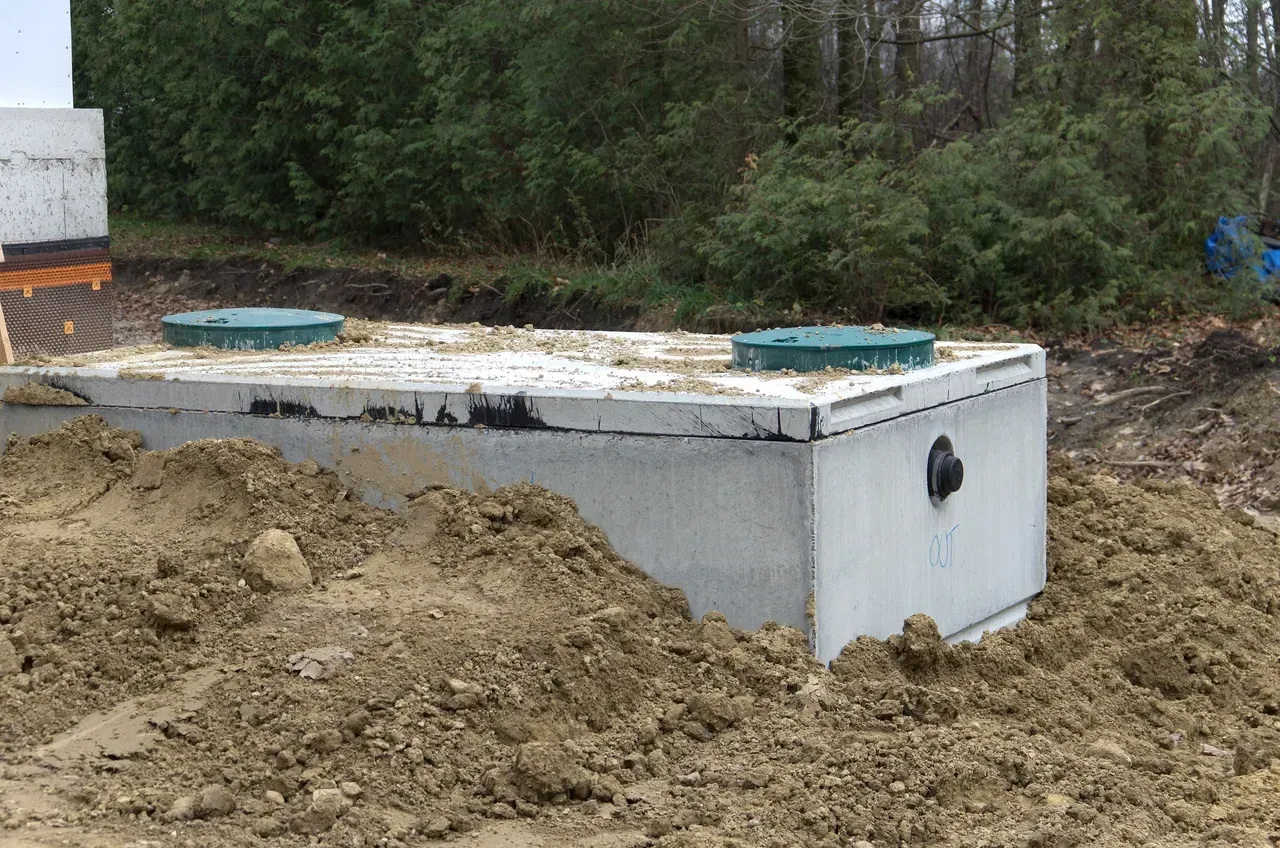 Concrete septic tank partially buried in dirt, with two green access covers.