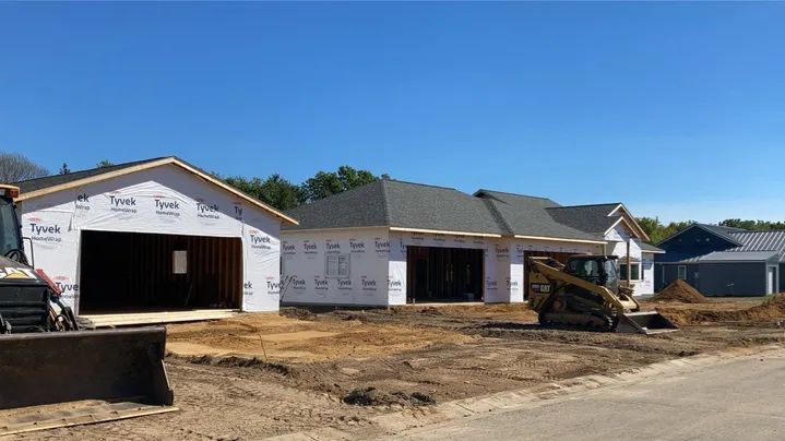New houses under construction with blue wrap, brown roofs, and earthmoving equipment.