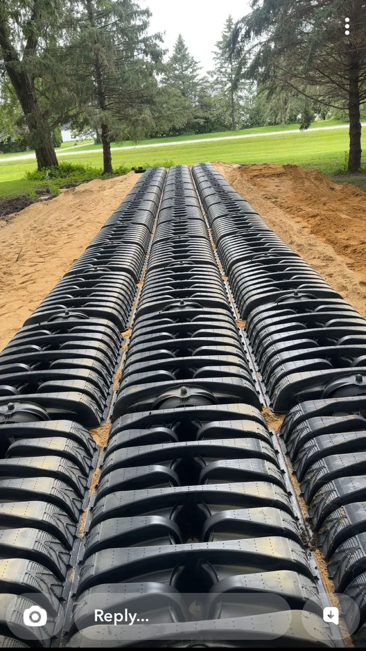 Black plastic septic tank field installation in a sandy trench. Green trees and grass background.