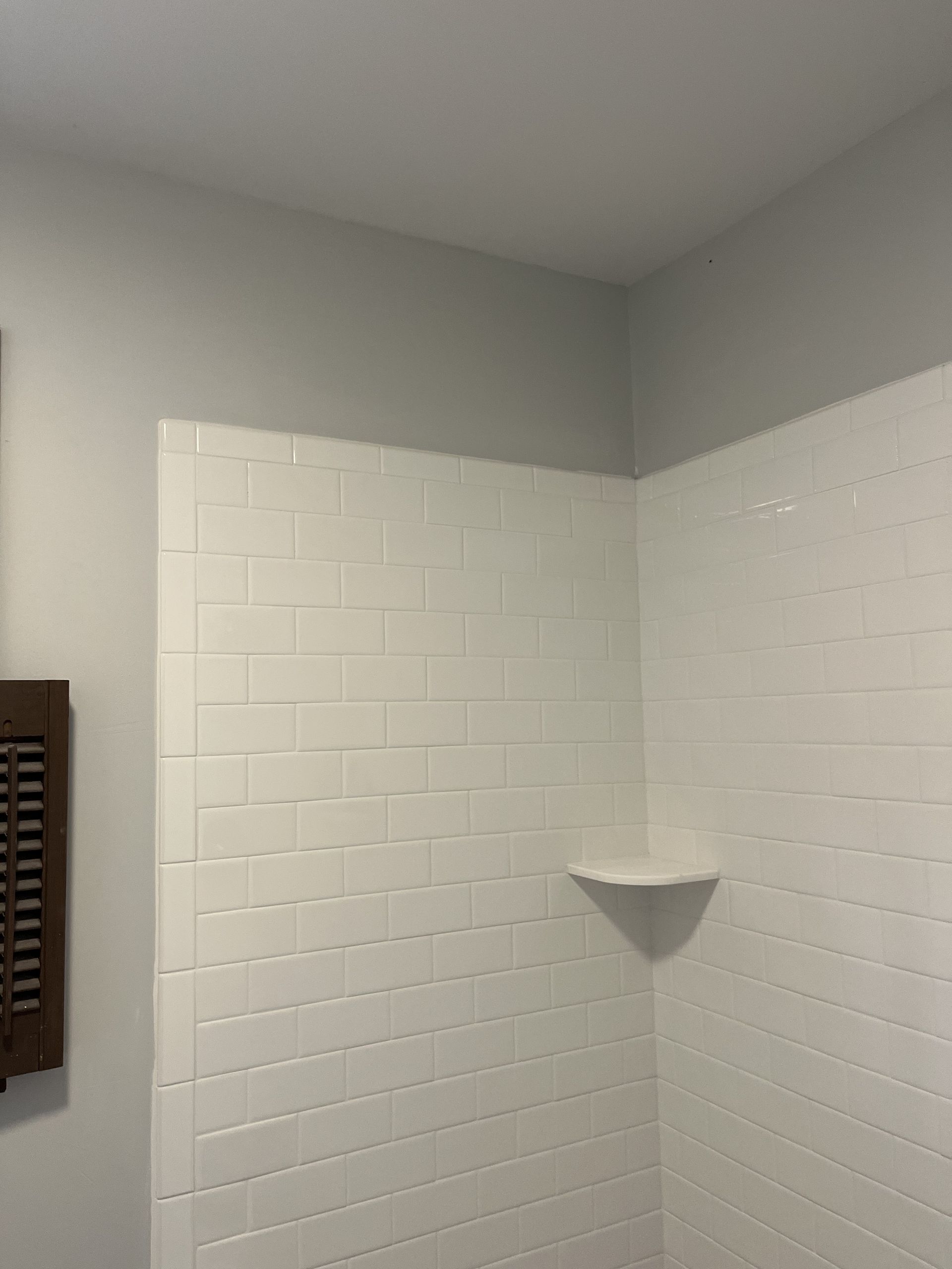 A bathroom with white tiles and a shelf in the corner.