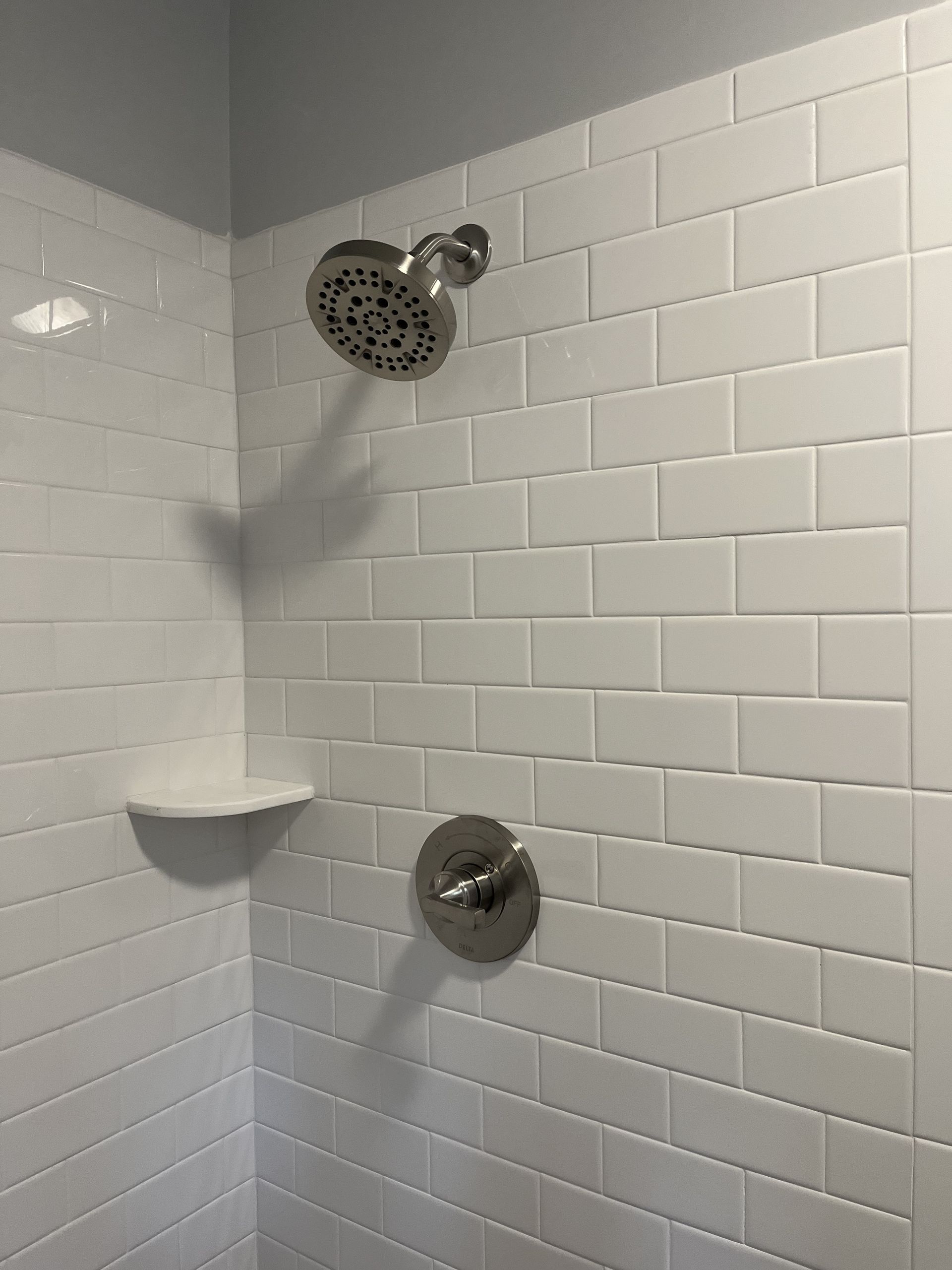 A shower with white tiles and a shower head.
