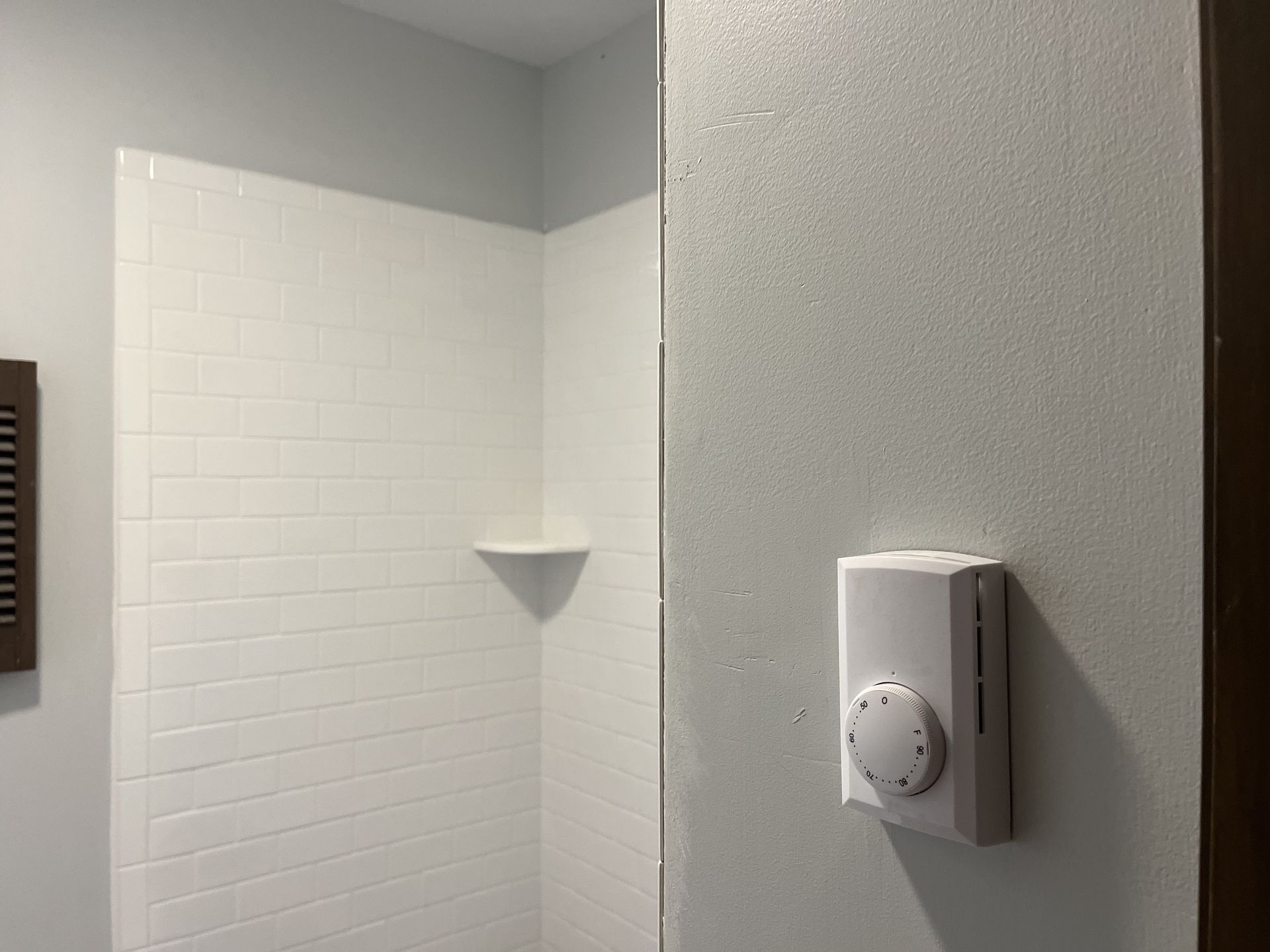 A bathroom with a shower and a thermostat on the wall.