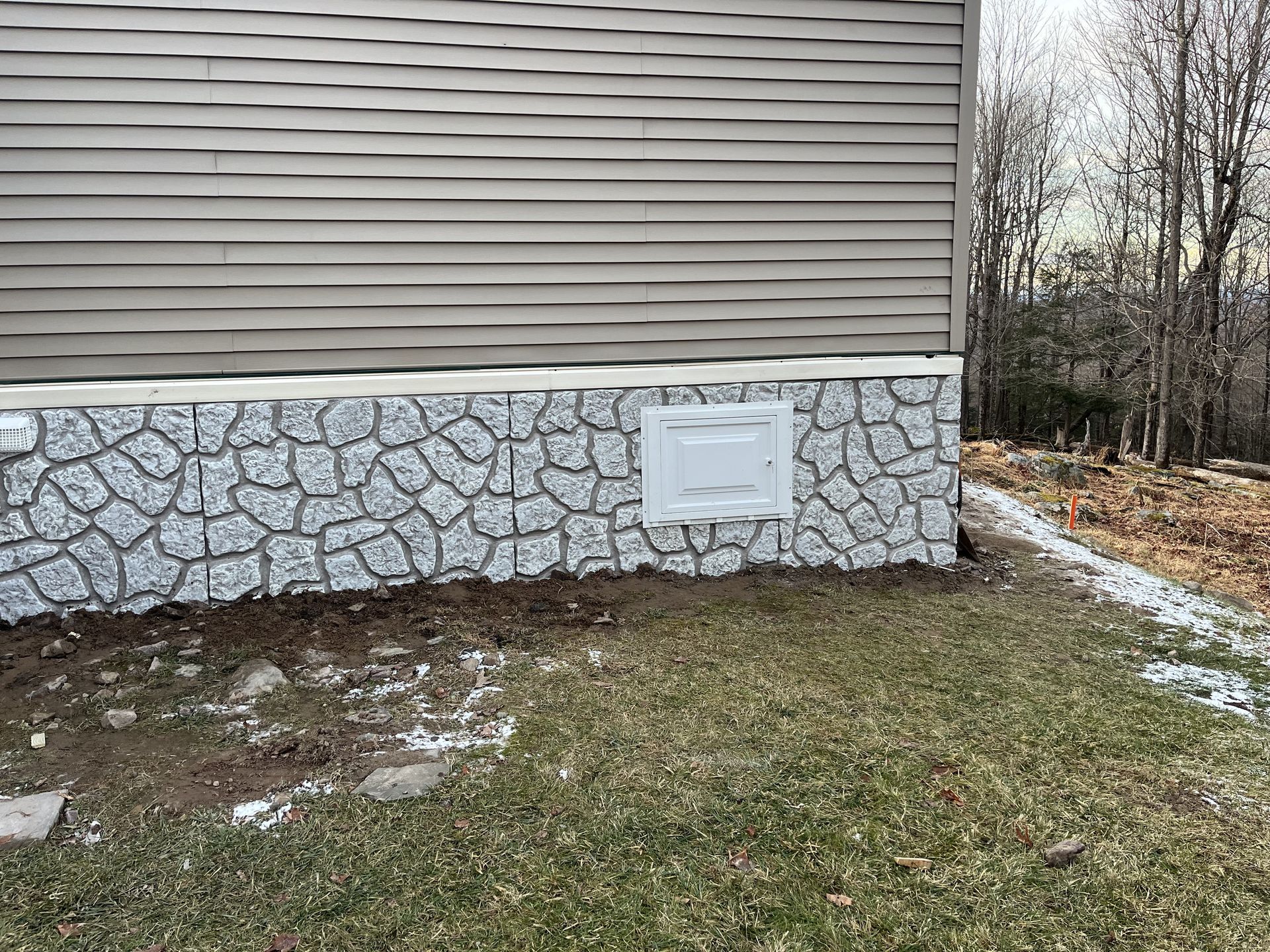 The side of a house with a stone wall and a window.