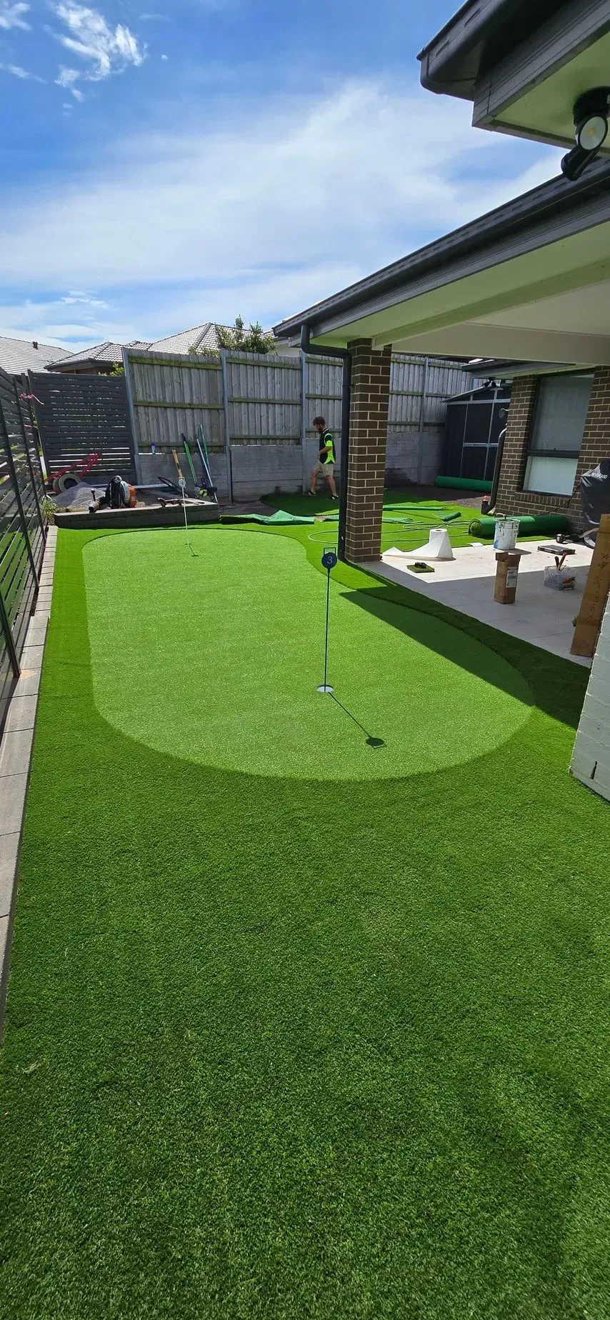 Artificial turf putting green in a backyard, with golf ball and flag visible.