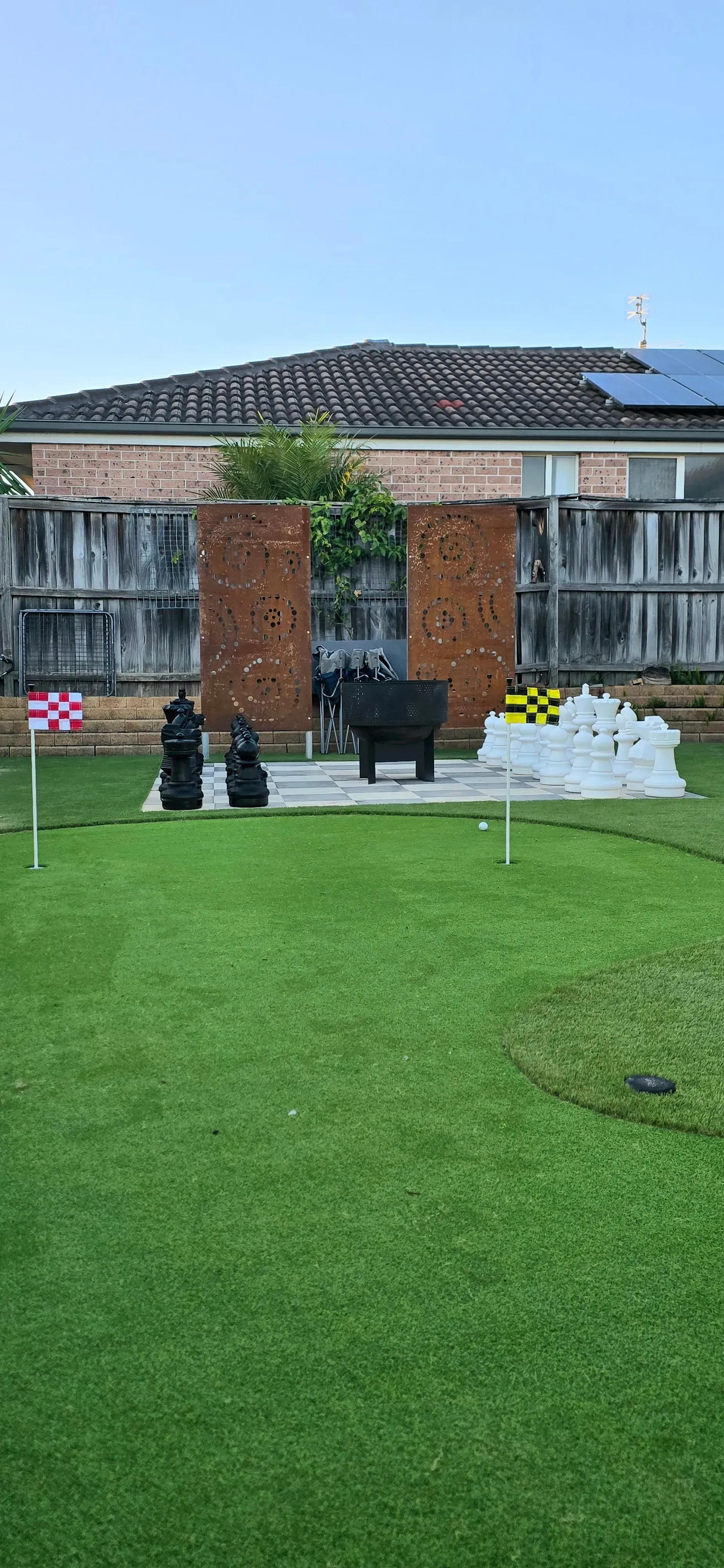 A backyard miniature golf course with artificial green grass, stone structures, and a wooden fence.