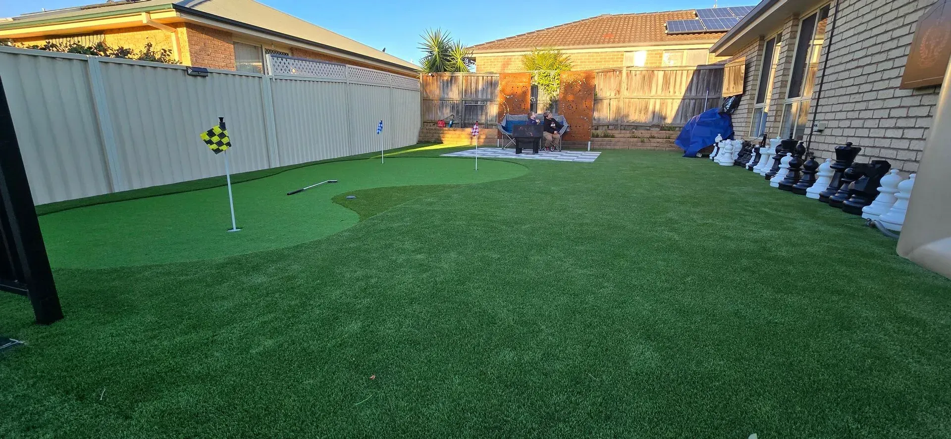 Backyard with artificial green turf, golf flags, and a line of decorative statues along a brick wall.