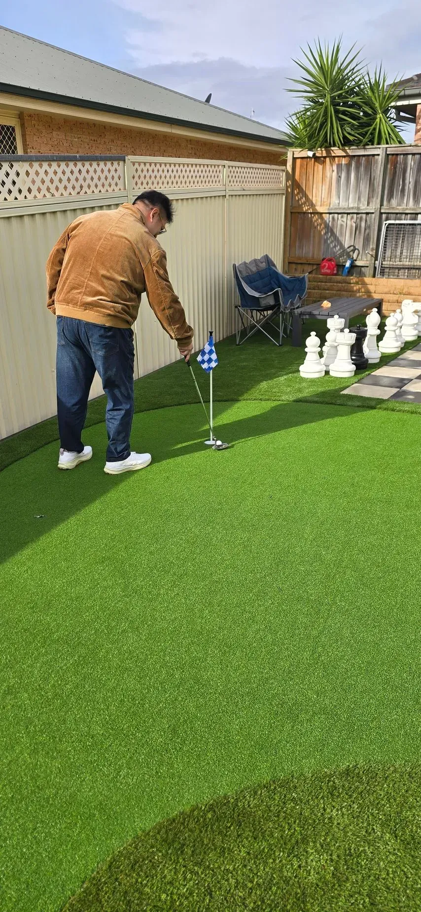 A person stands on a green lawn, looking at a small golf flag, near giant chess pieces.
