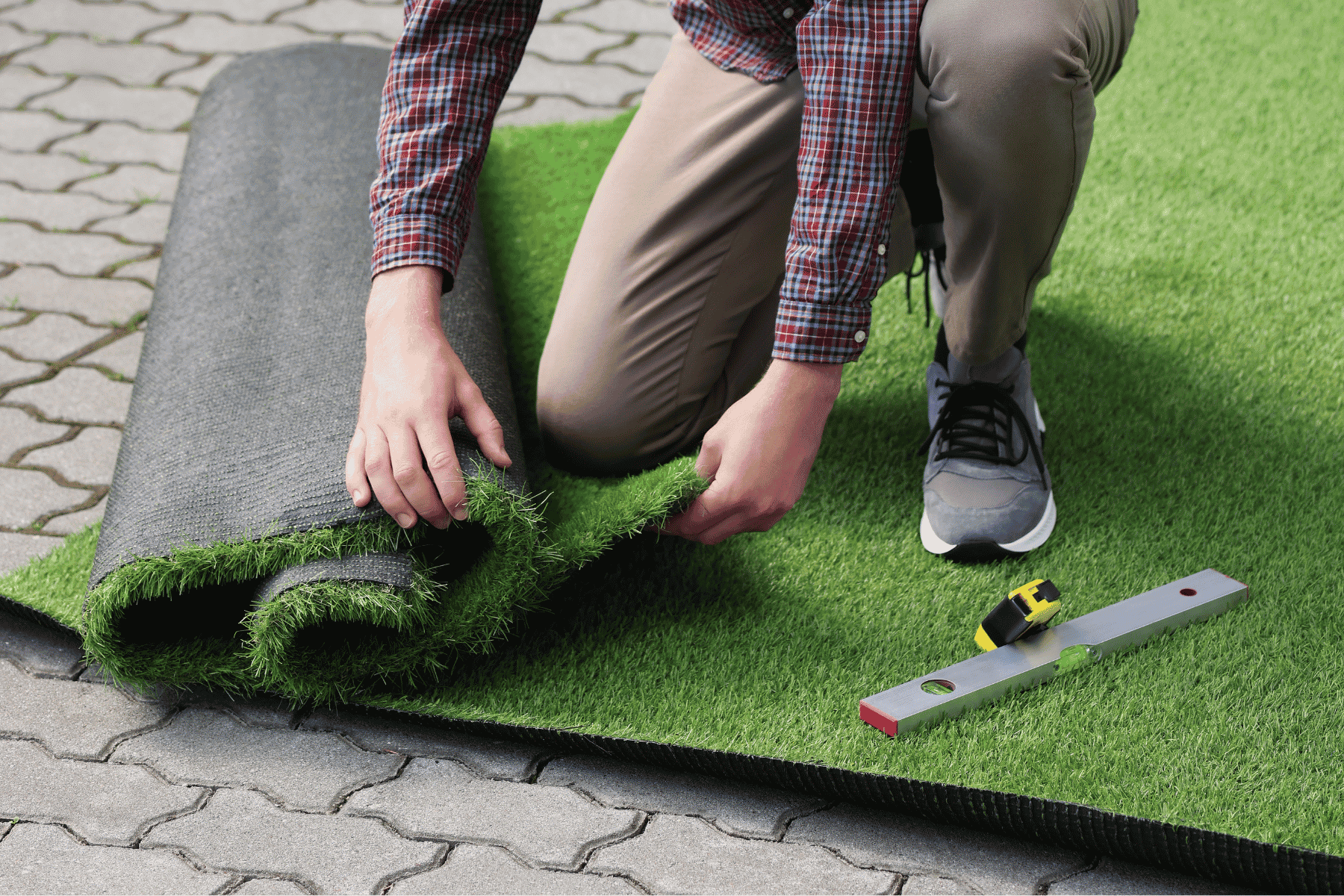 A man is installing green synthetic grass, carefully laying it out on a surface for a neat finish.