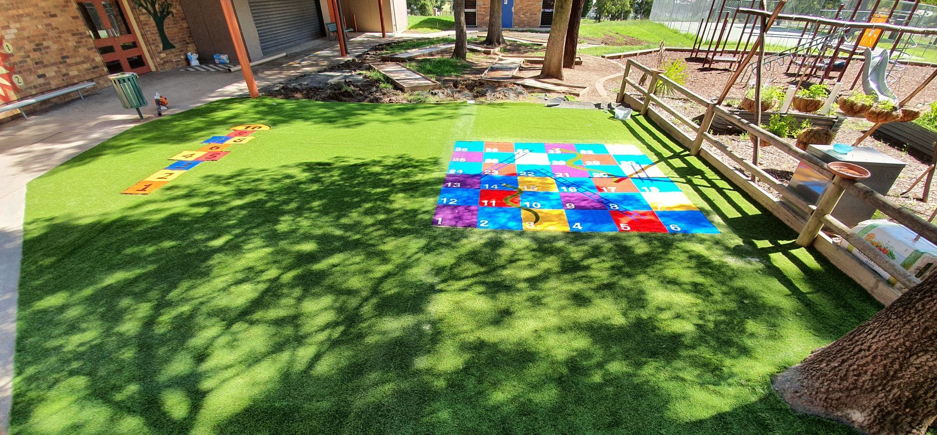 A colorful playground with a grass area featuring a hopscotch game and a block activity.