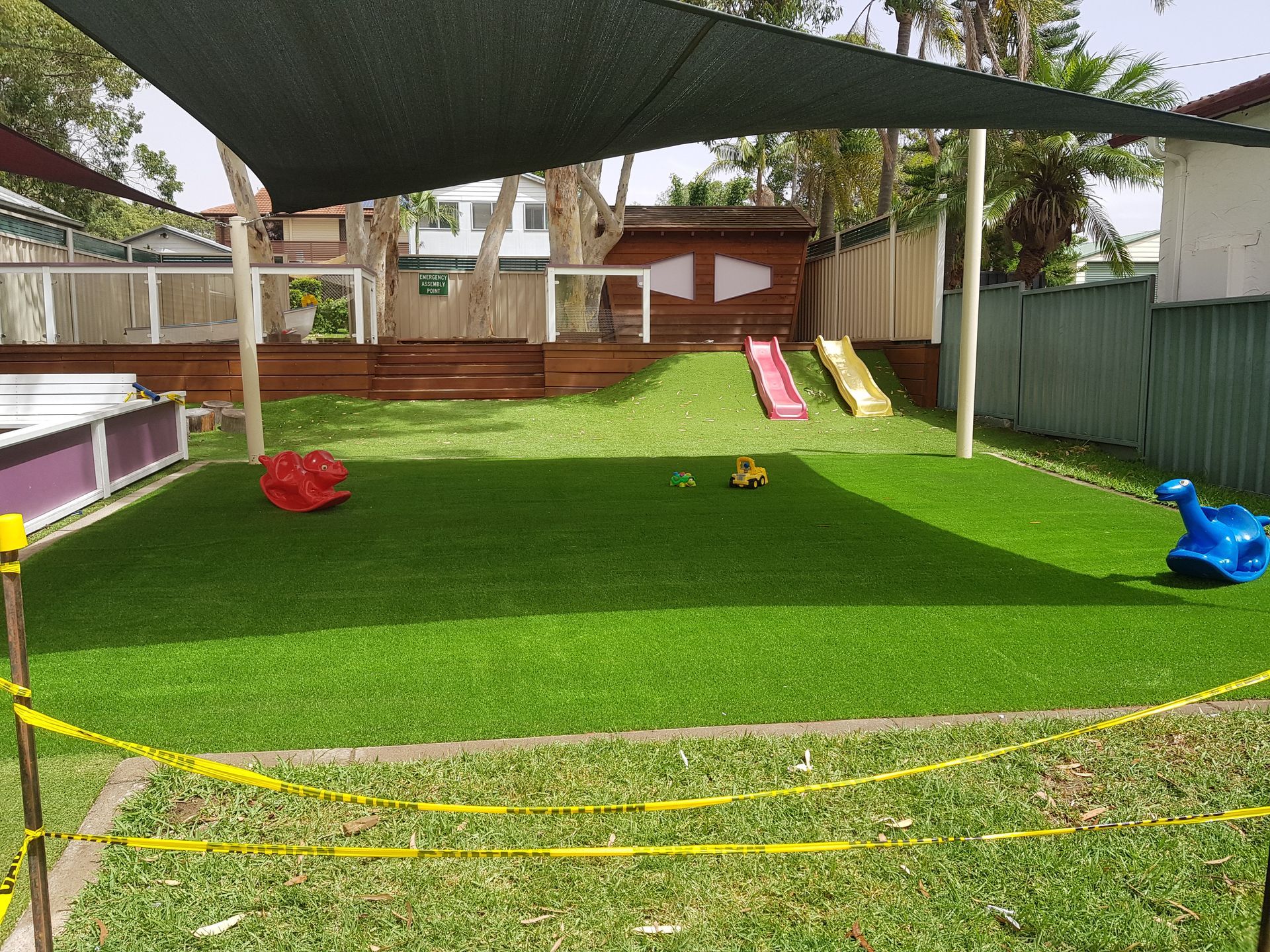 Playground with green turf, slides, toys, and shade sails.