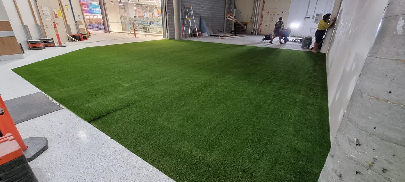 Indoor space with artificial turf, people near a climbing wall, and construction materials.