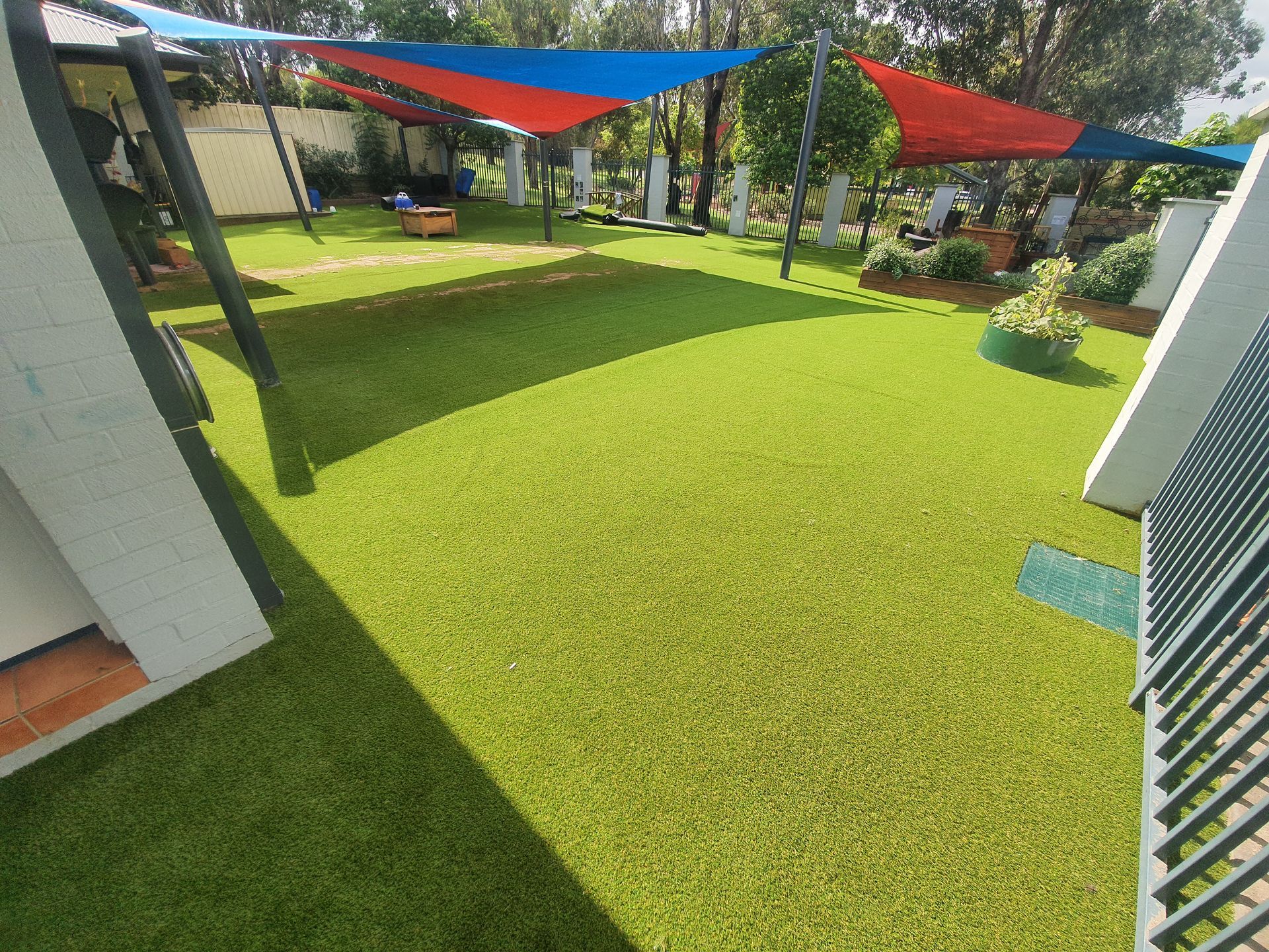 Green artificial turf under a red and blue shade cloth at a daycare center.