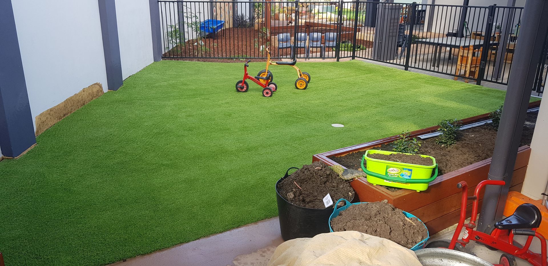 A small artificial turf yard with two children's riding toys. Walls and a fence surround the yard.