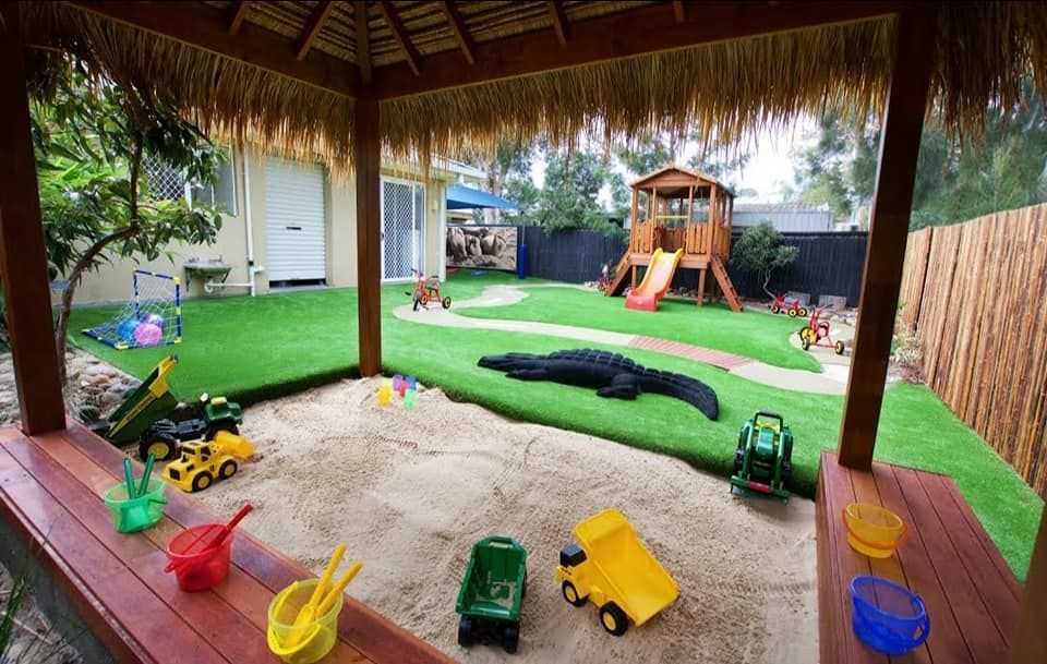 Playground with sandpit, toys, grass, and wooden playhouse.