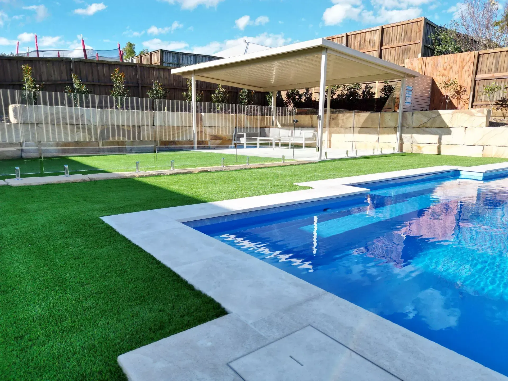 A pool with a blue interior, adjacent green lawn, and a shaded outdoor seating area.