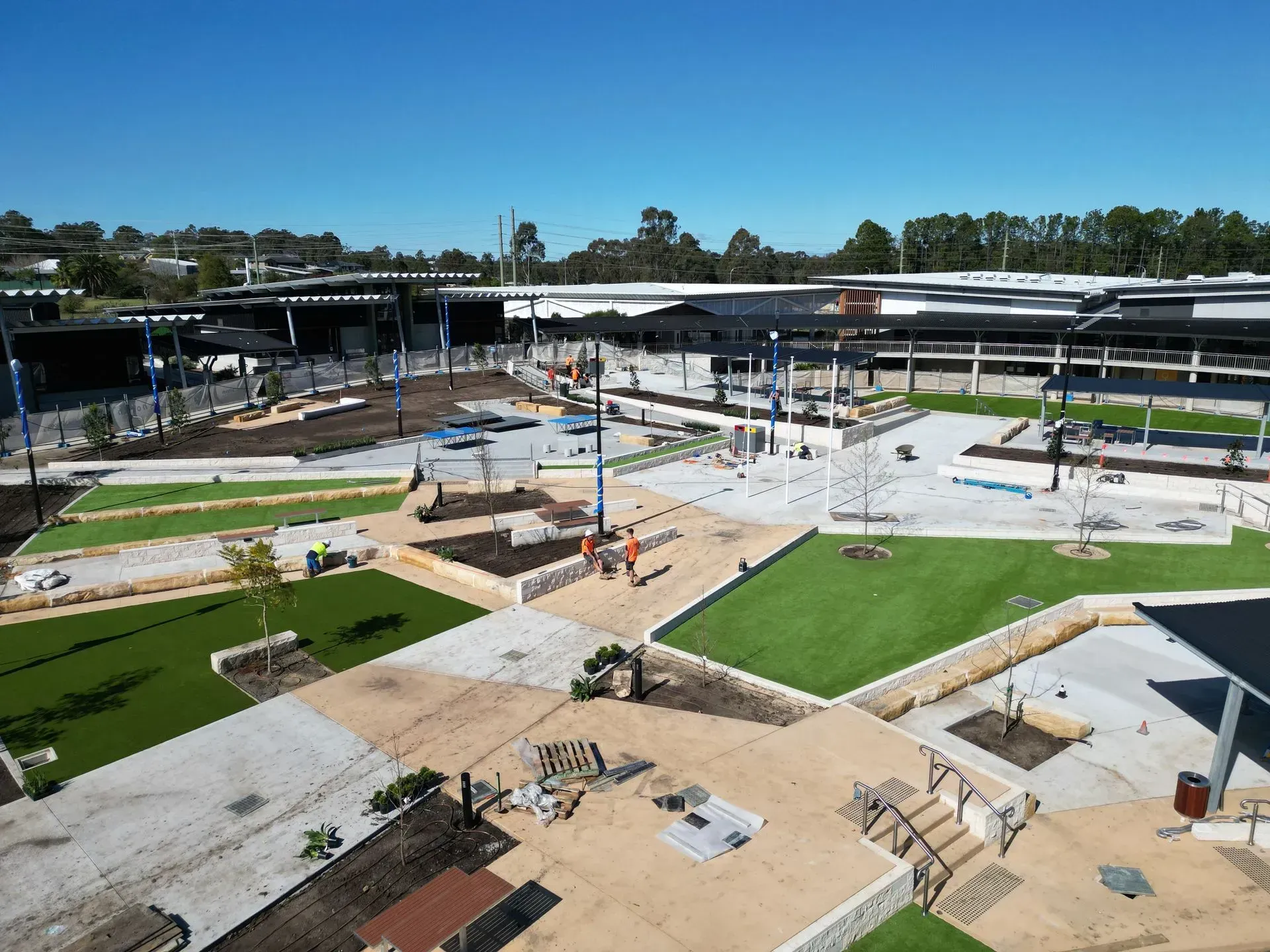 Construction site: outdoor plaza with landscaping, buildings in background, blue sky.