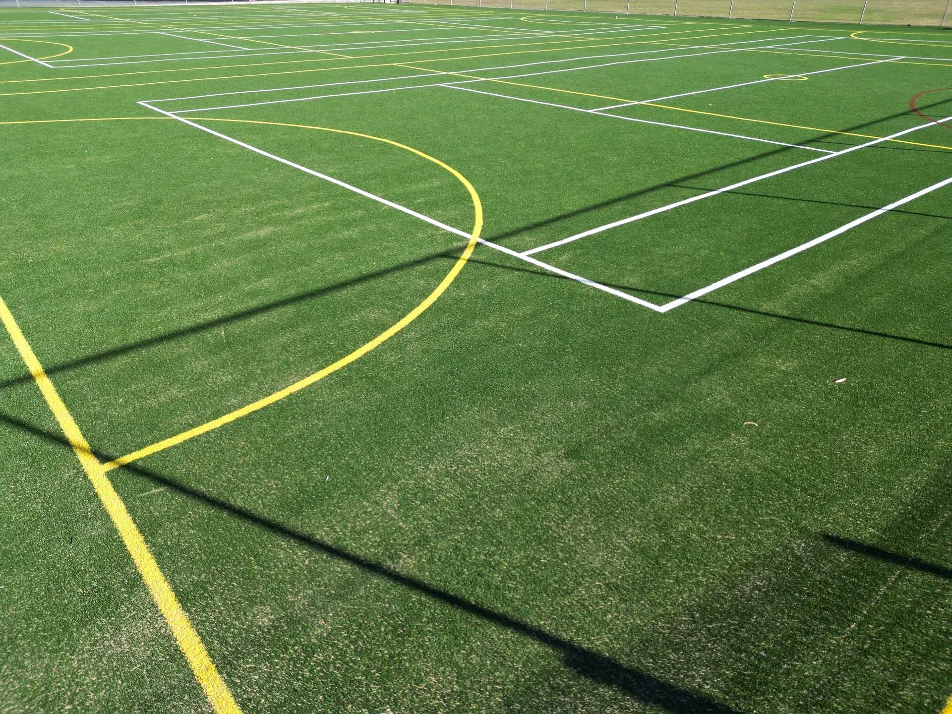 Green artificial turf field with white and yellow markings for sports.