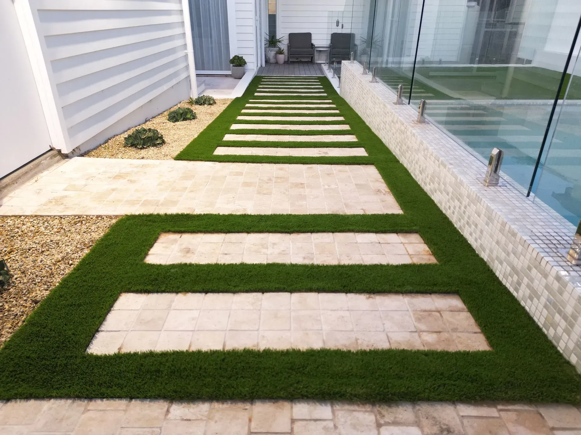 Stone pathway with square stepping stones framed by green turf, leading to chairs.