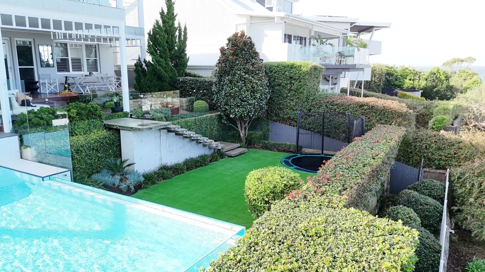 Backyard with pool, artificial lawn, hedges, and coastal homes.
