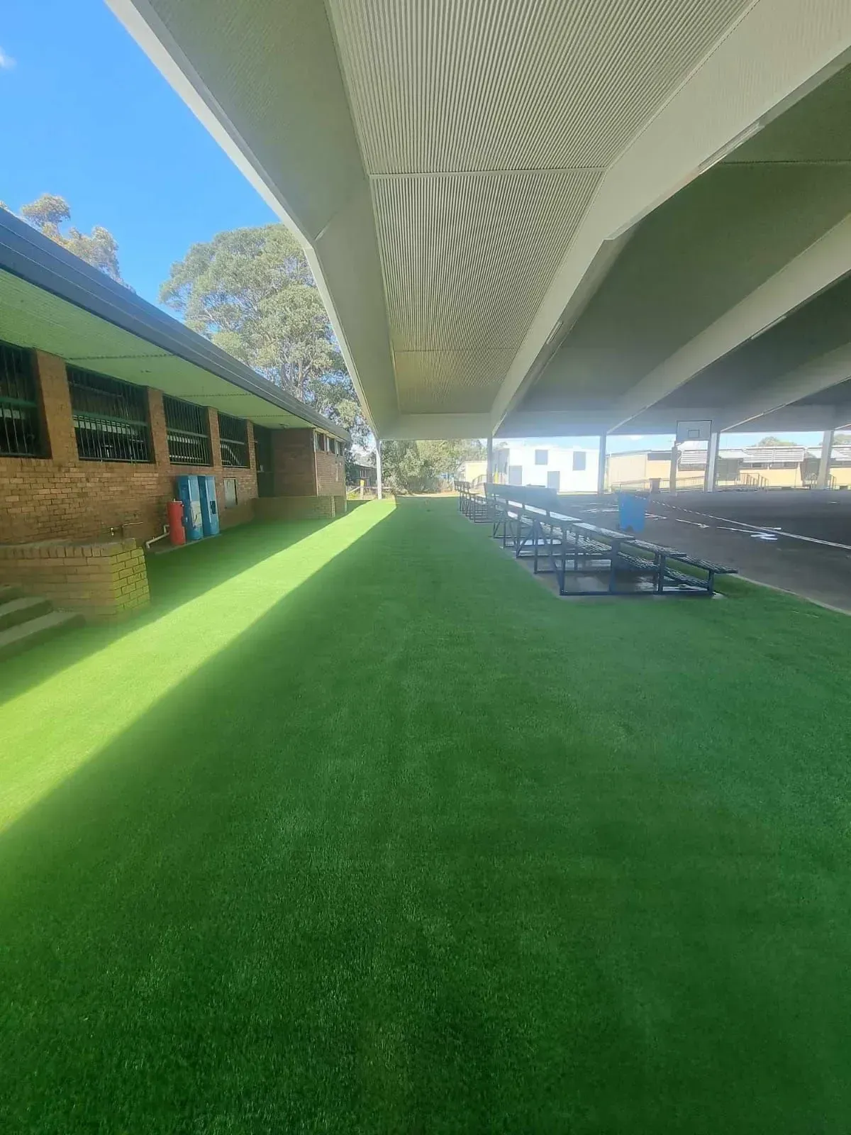 Artificial turf under a covered walkway at an outdoor area with a brick building on the left.