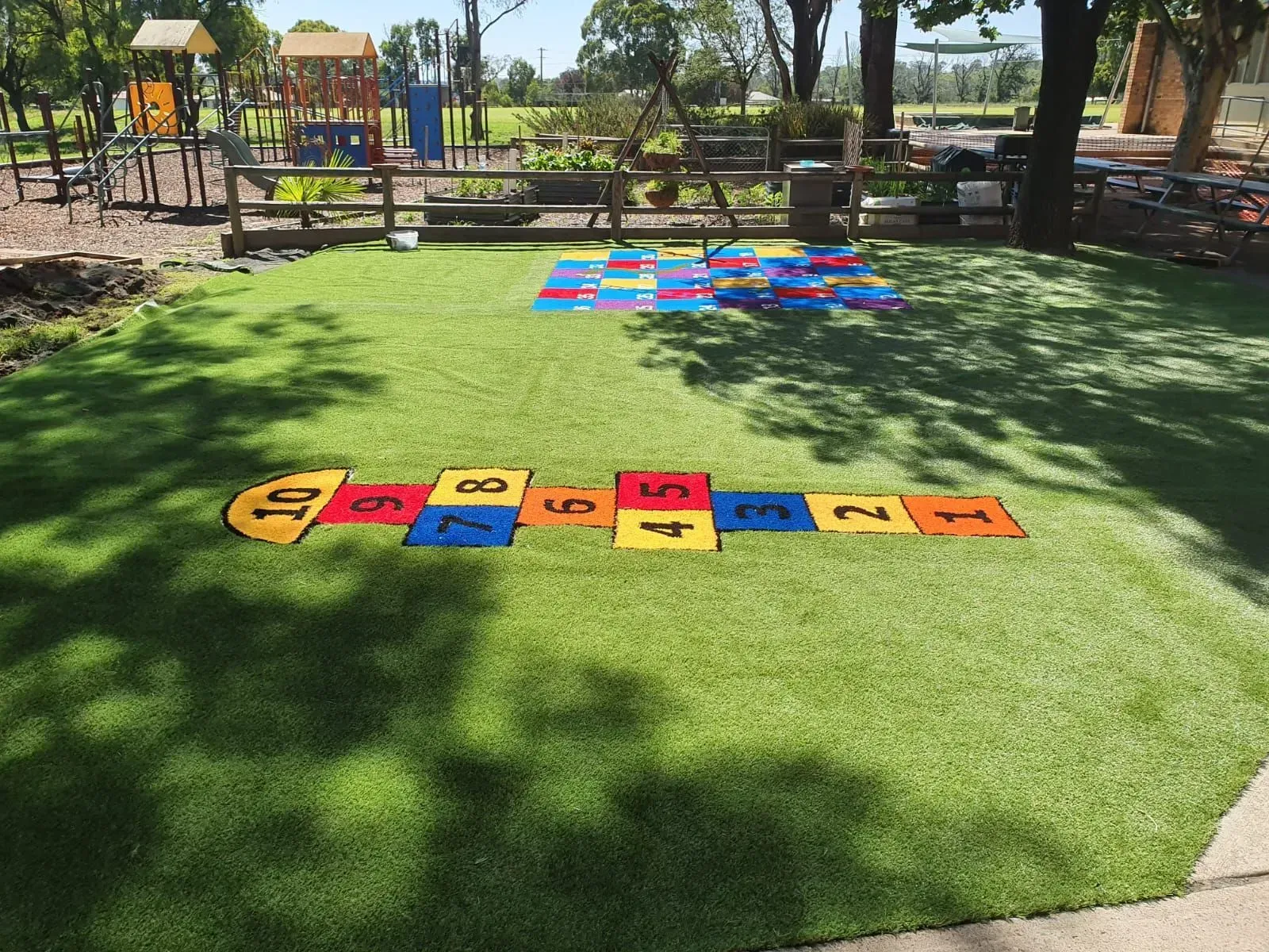 Hopscotch and colorful mats on green artificial turf at a playground.