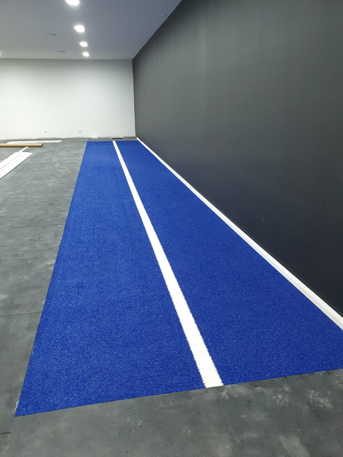 Blue artificial turf runway with white lines, beside a black wall.