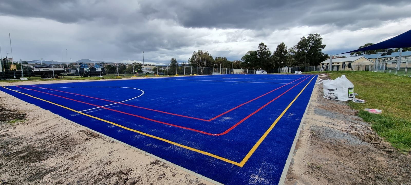 Blue sports field with white lines, under cloudy sky.