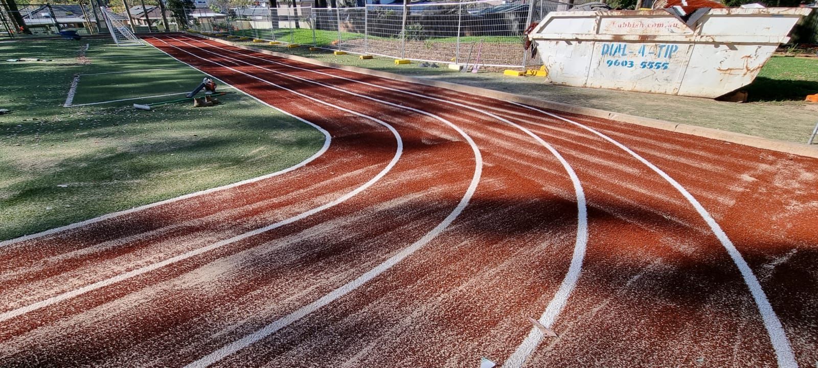 A red running track with white lane lines curves to the right, next to green grass.