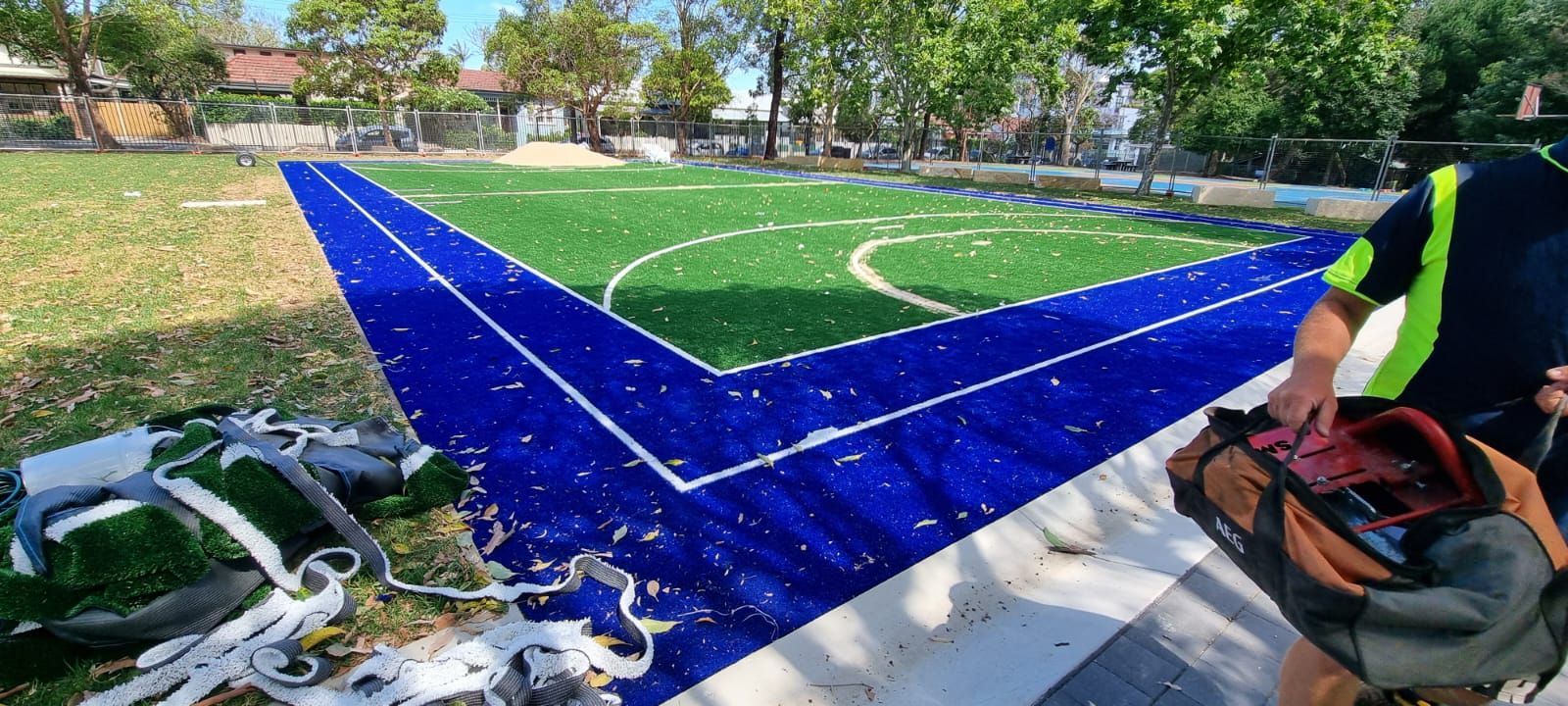 A newly installed turf sports court with blue border, a person opening a bag.