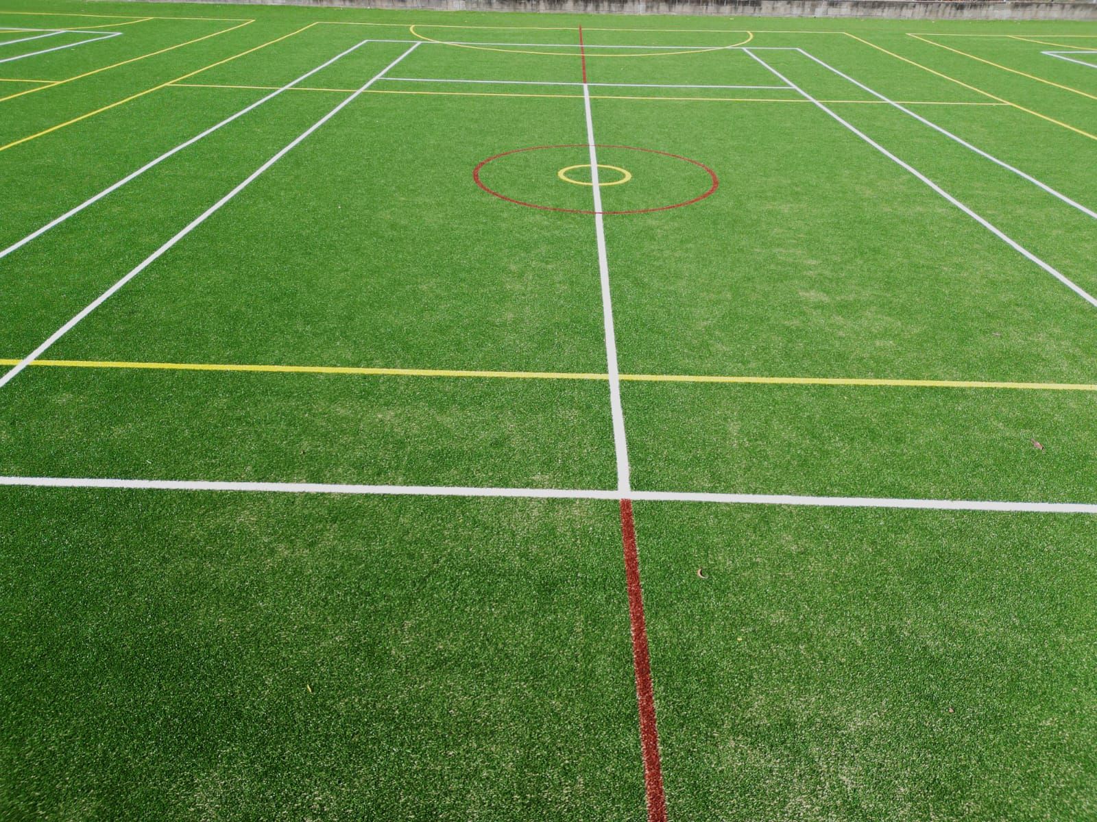 Green artificial turf field with white, yellow, and red lines, and a center circle.
