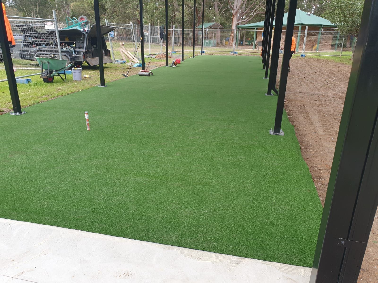 Green artificial turf pathway under a black metal structure, construction site backdrop.