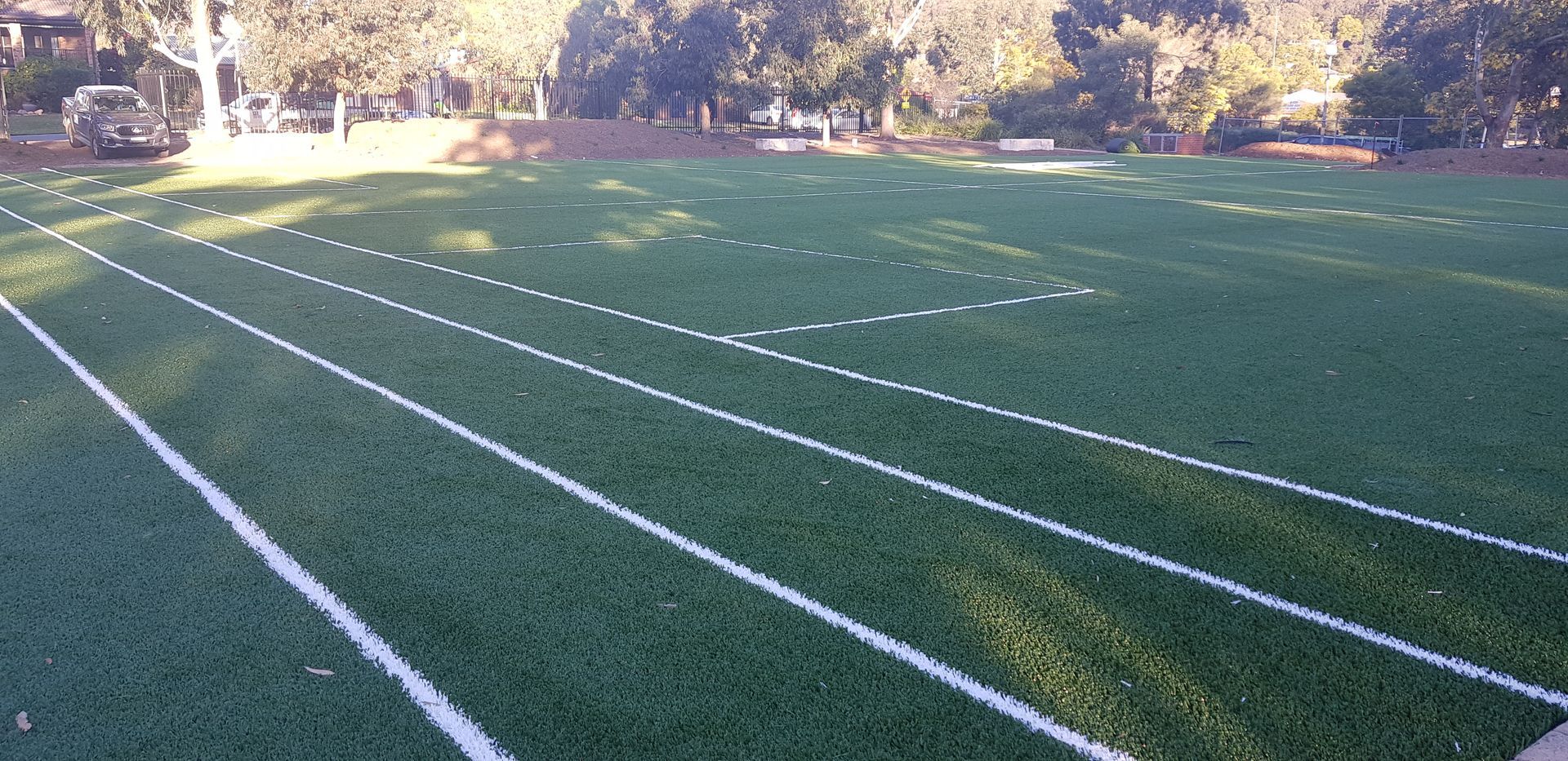 Green turf track with white lane markings, trees in background.