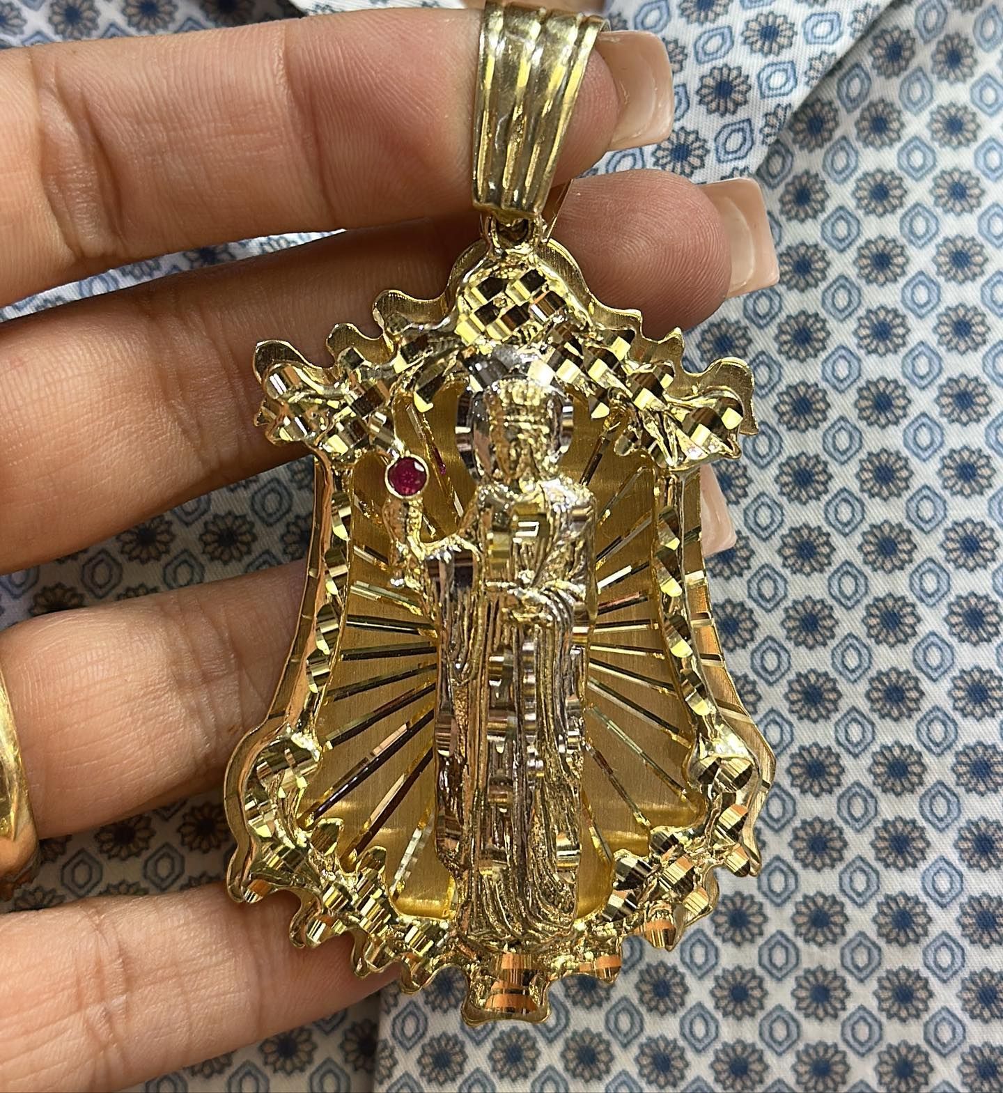 Una persona sostiene un colgante de oro con Jesús en él. Yene Joyeria