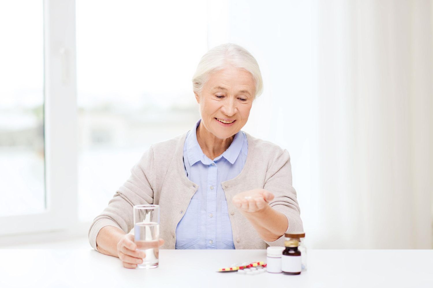 An elderly woman is sitting at a table taking pills.