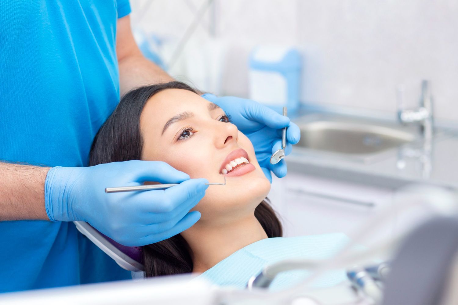 A woman is sitting in a dental chair while a dentist examines her teeth.