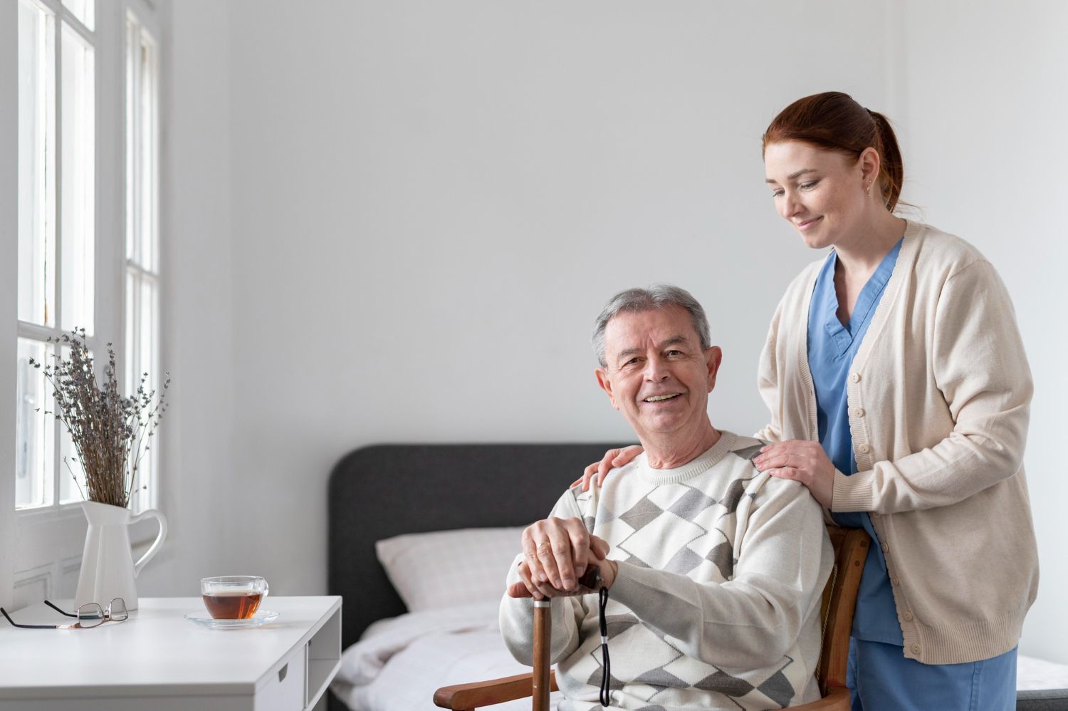An elderly man is sitting in a chair with a cane and a nurse is standing next to him.