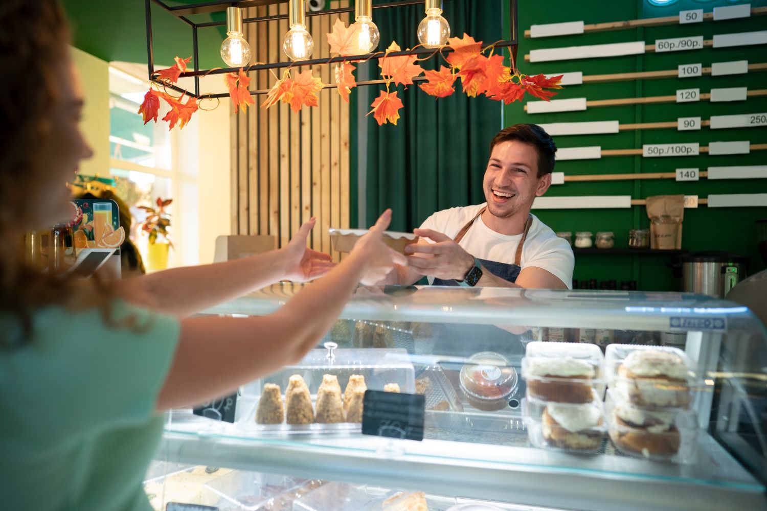 A woman is standing in front of a display case in a bakery.