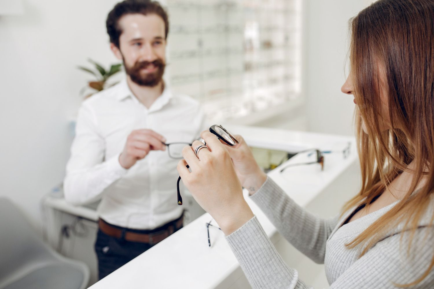 A woman is holding a pair of glasses in front of a man in an optical shop.