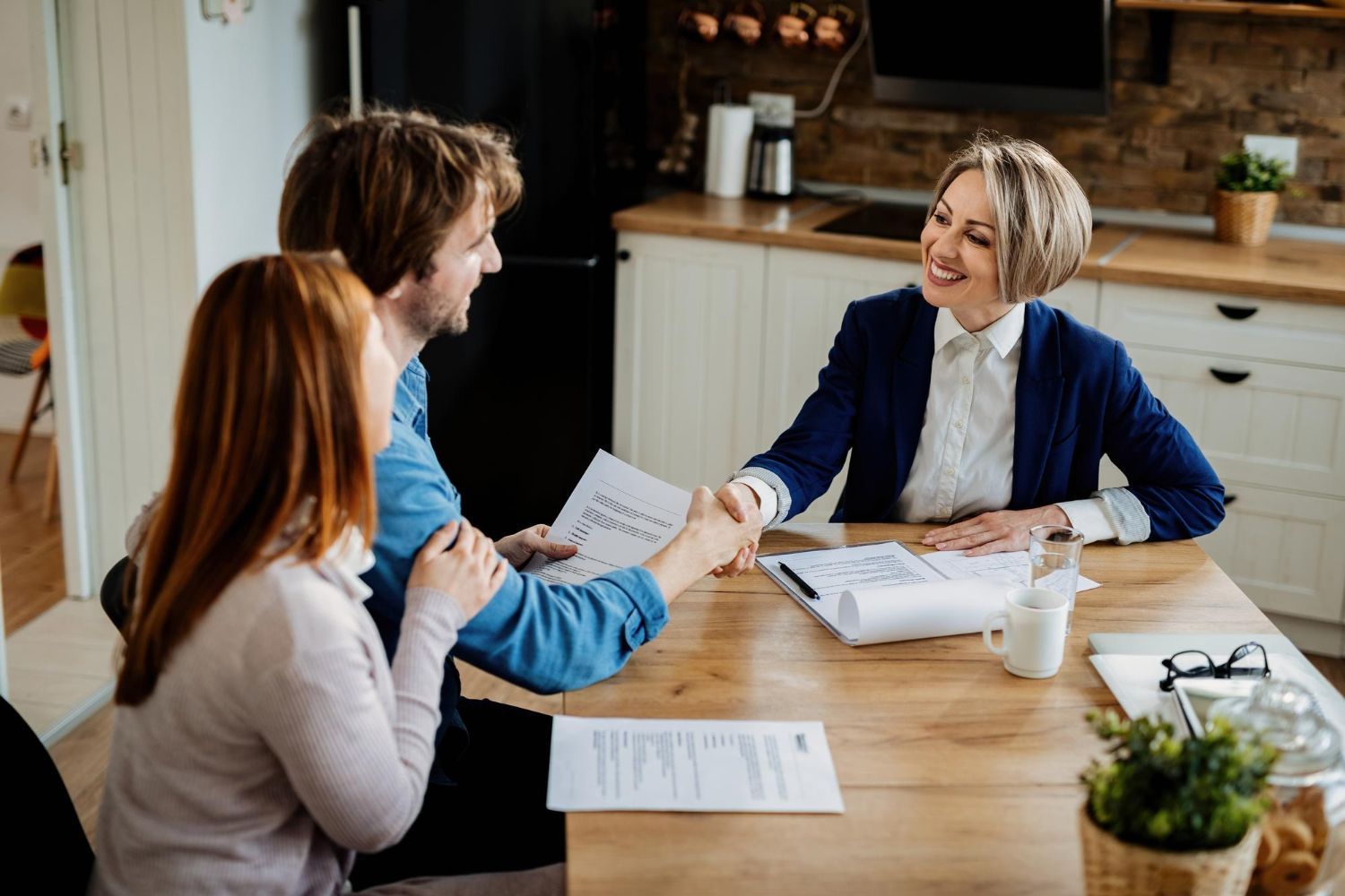 A woman is shaking hands with a man and a woman while sitting at a table.
